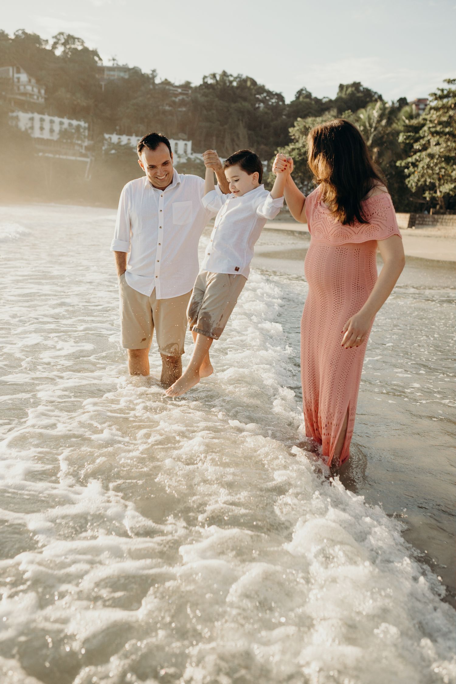 Family playing in ocean waves during sunset at a coastal beach.