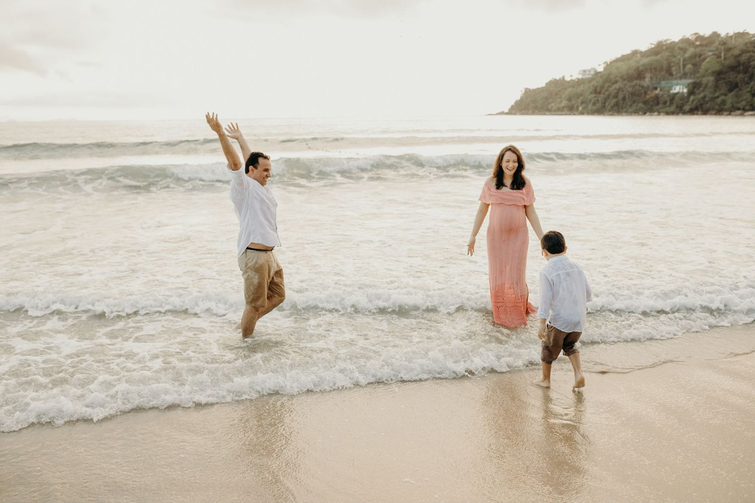A family having fun and jumping in the shallow ocean waves at sunset.