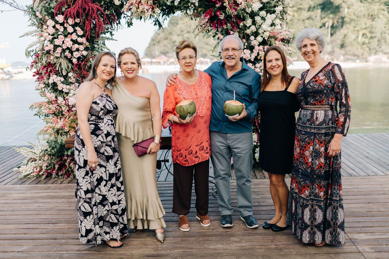 Wedding guests gather for group photos on decorated wooden deck by the lake.