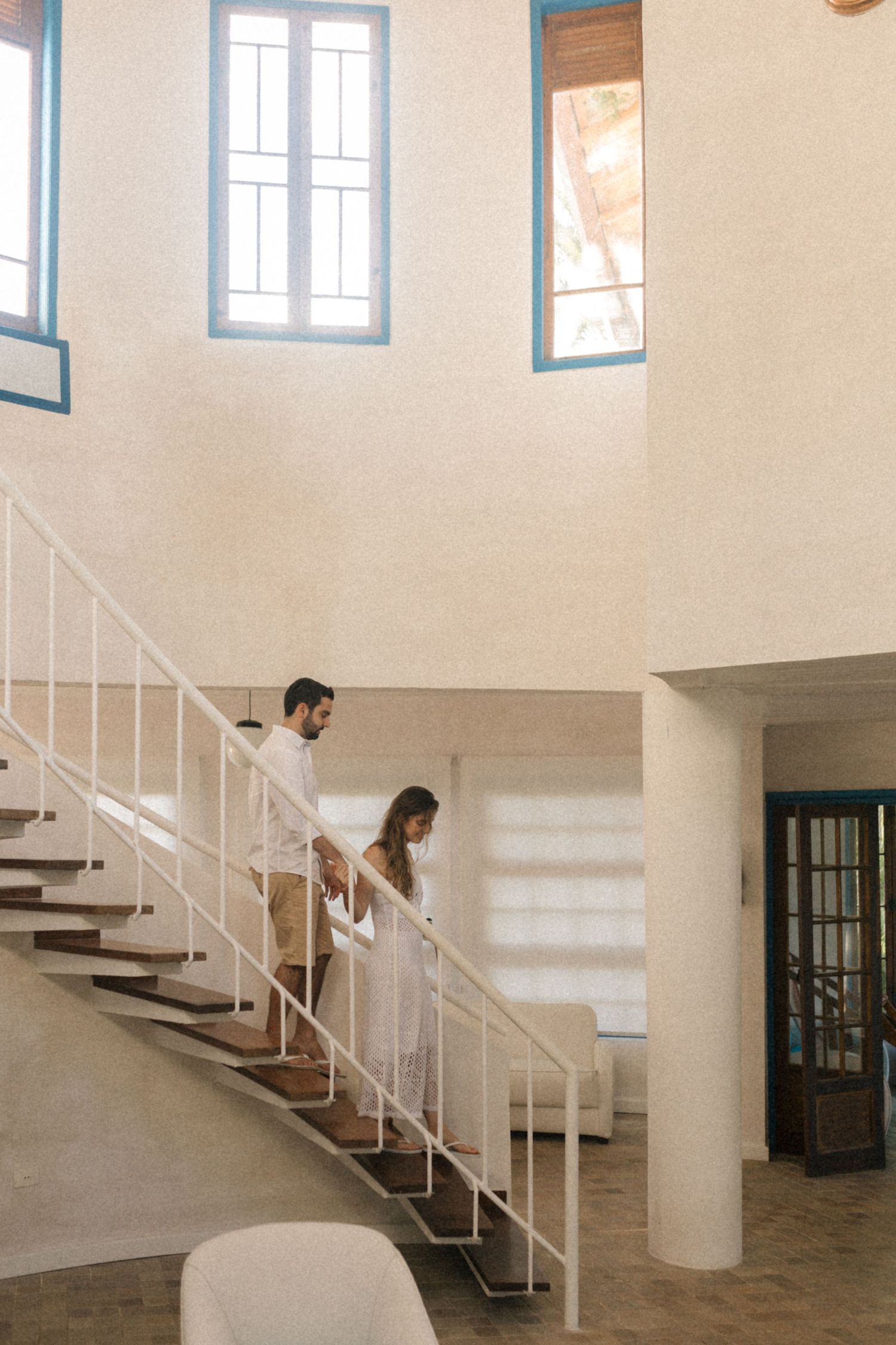Couple descending white staircase in bright modern interior with blue windows.