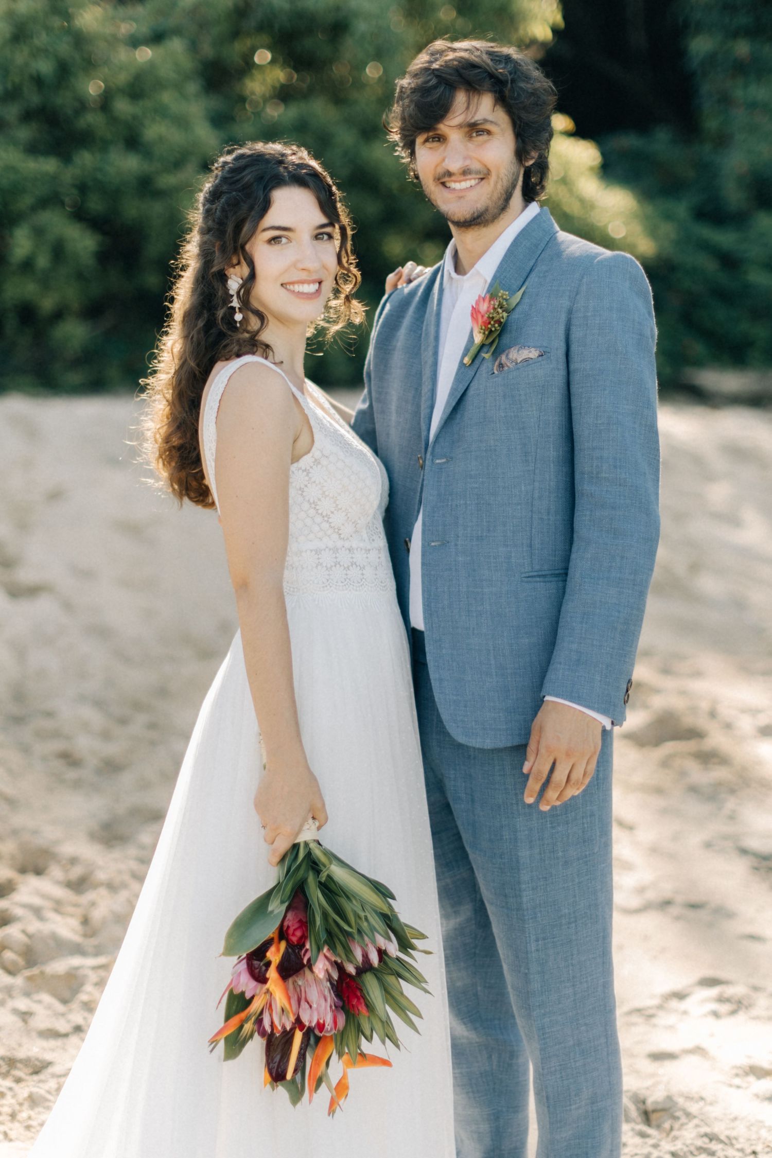 Candid wedding portraits of couple on beach with bride holding vibrant tulip bouquet.