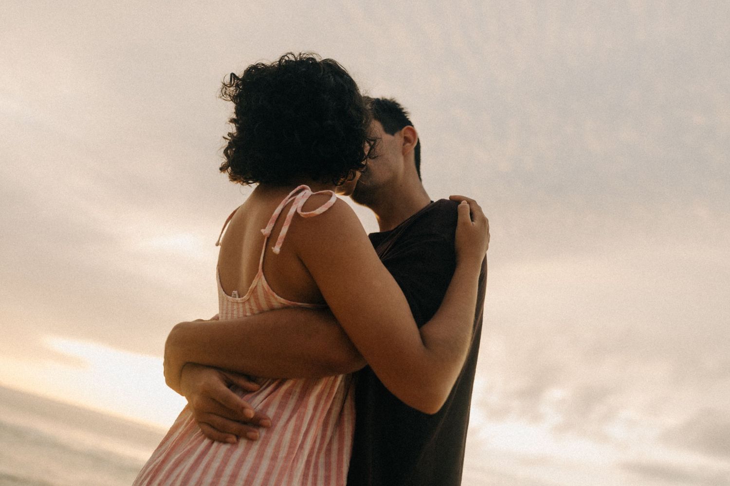 Um casal em um abraço terno recortado contra um céu quente do pôr do sol em uma noite de verão.
