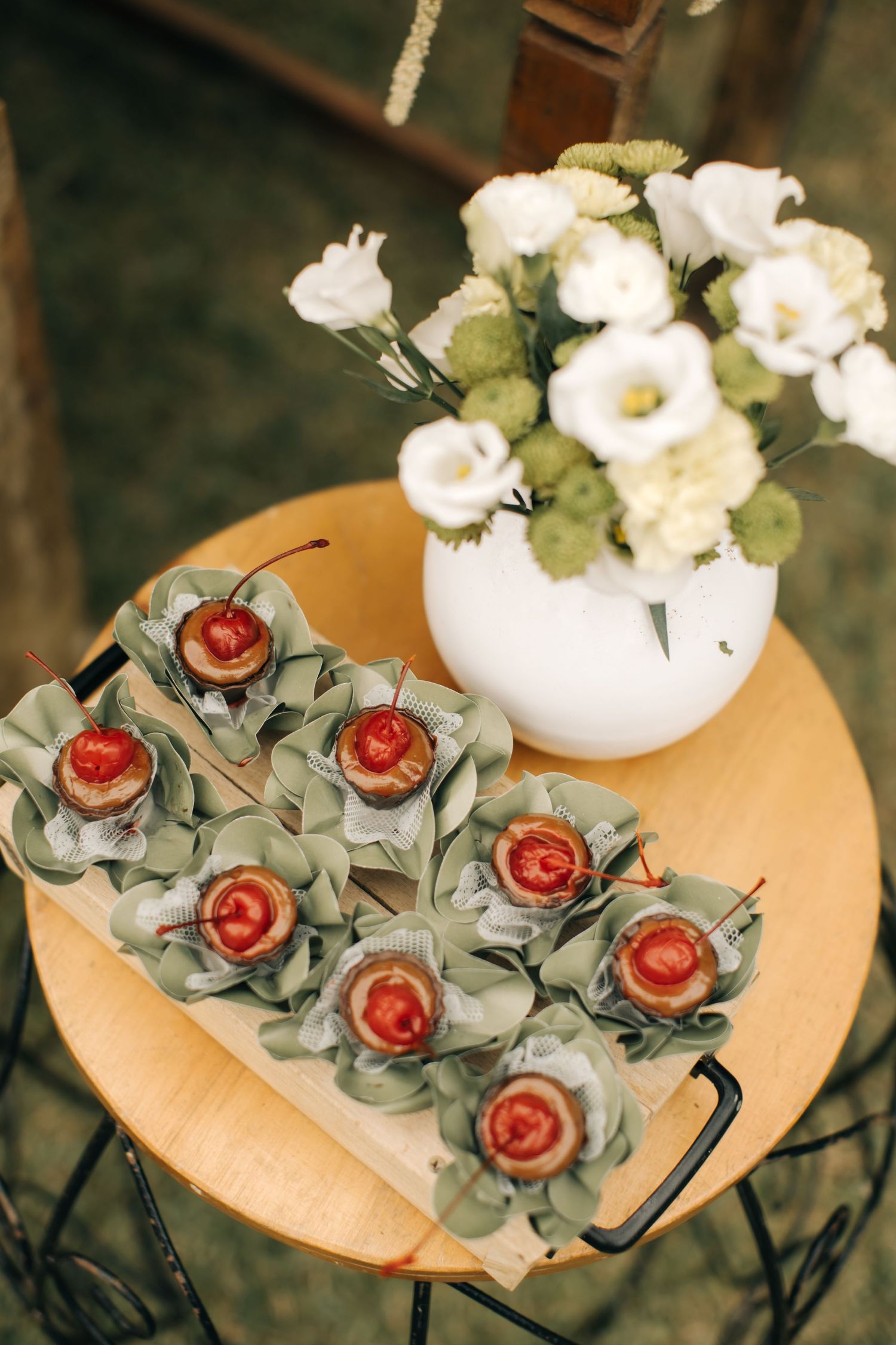 White flowers in round vase next to decorative rose-shaped appetizers on wooden plate.