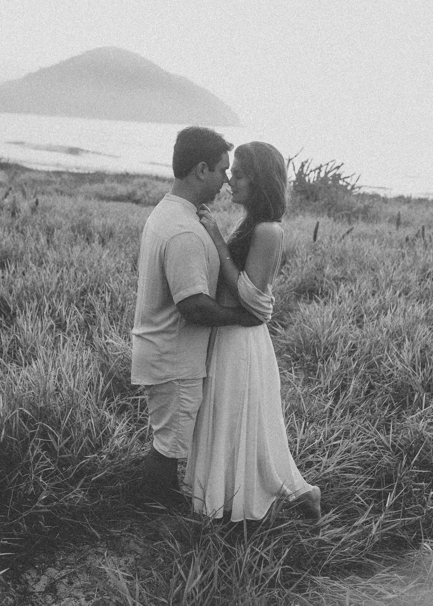 A couple embraces in a grassy hillside field during a romantic outdoor photoshoot.
