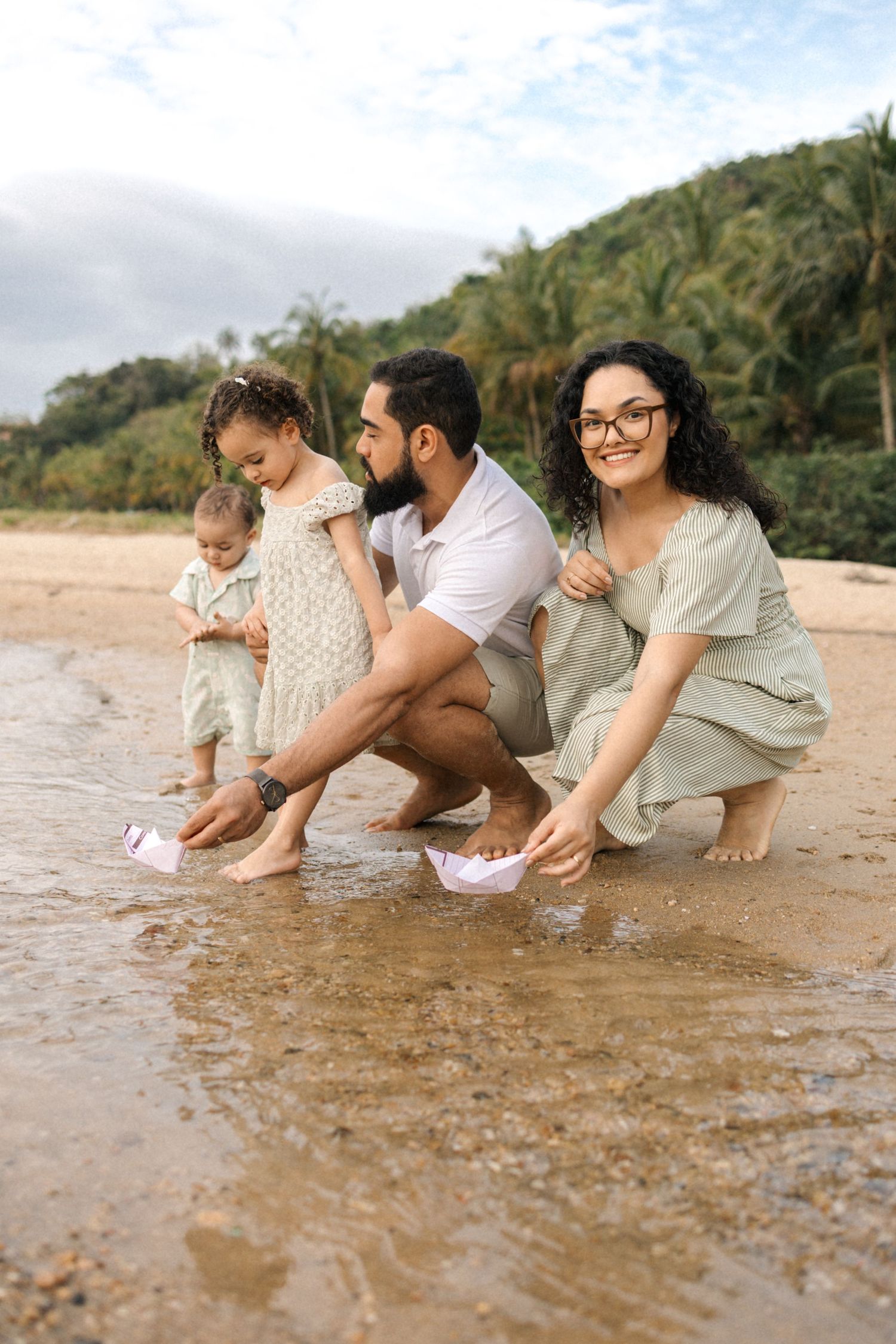 Family sitting together at the beach playing with sand and water on a sunny tropical day.