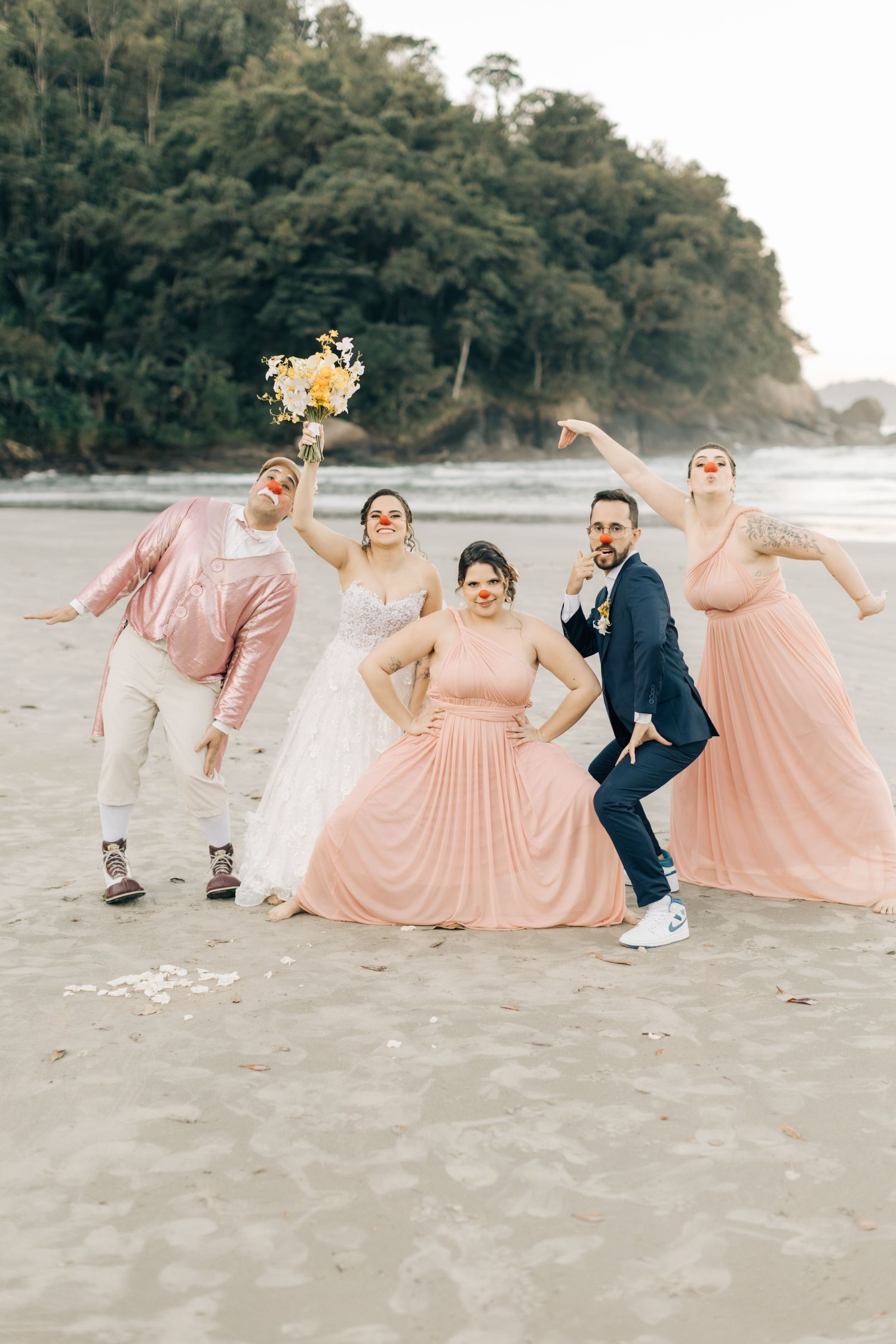 Fun bridal party photo with coordinating pink outfits on scenic beach.