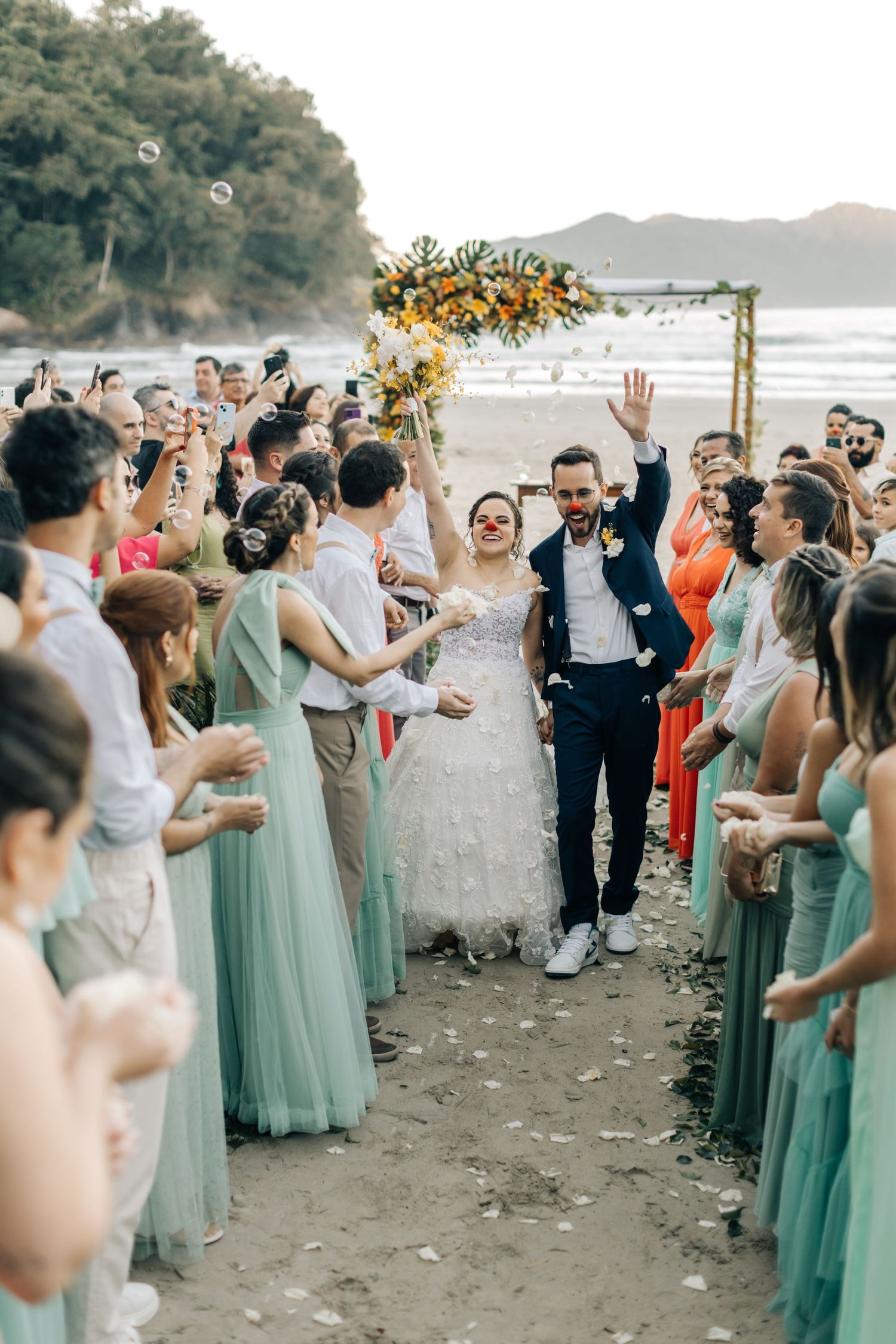 Wedding guests in mint green dresses celebrate on beach with newlyweds.