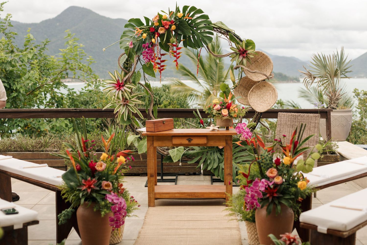 A tropical outdoor terrace decorated with colorful flowers and palm fronds overlooking mountain views.