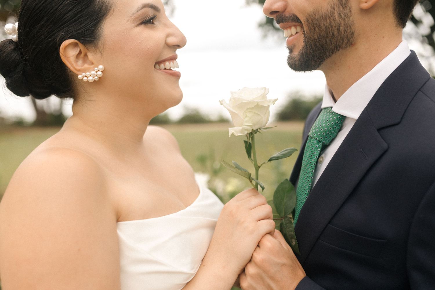 A romantic moment captured between newlyweds with a white rose and emerald green tie detail.