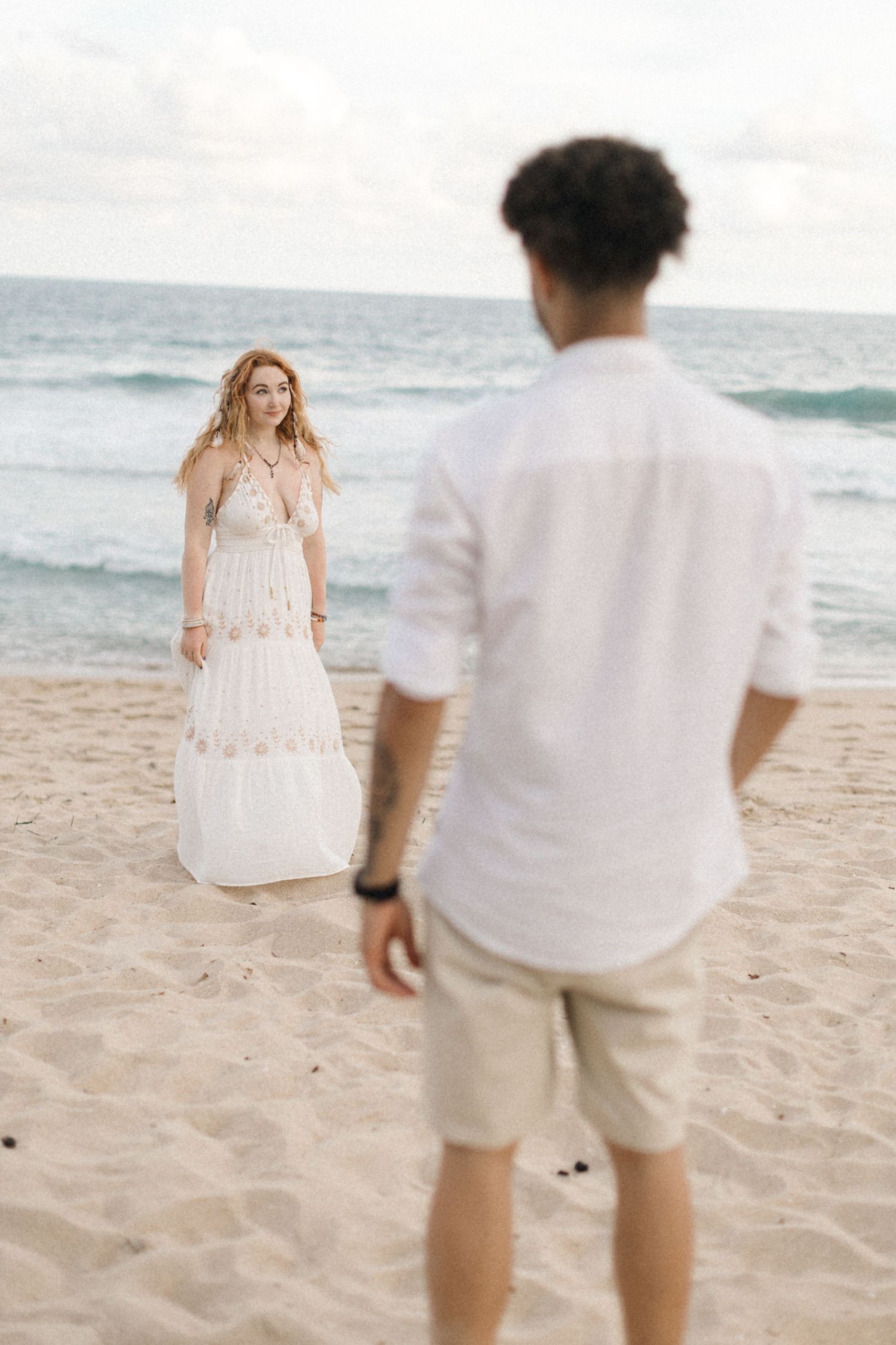 Couple in white outfits having a playful moment on a scenic beach.