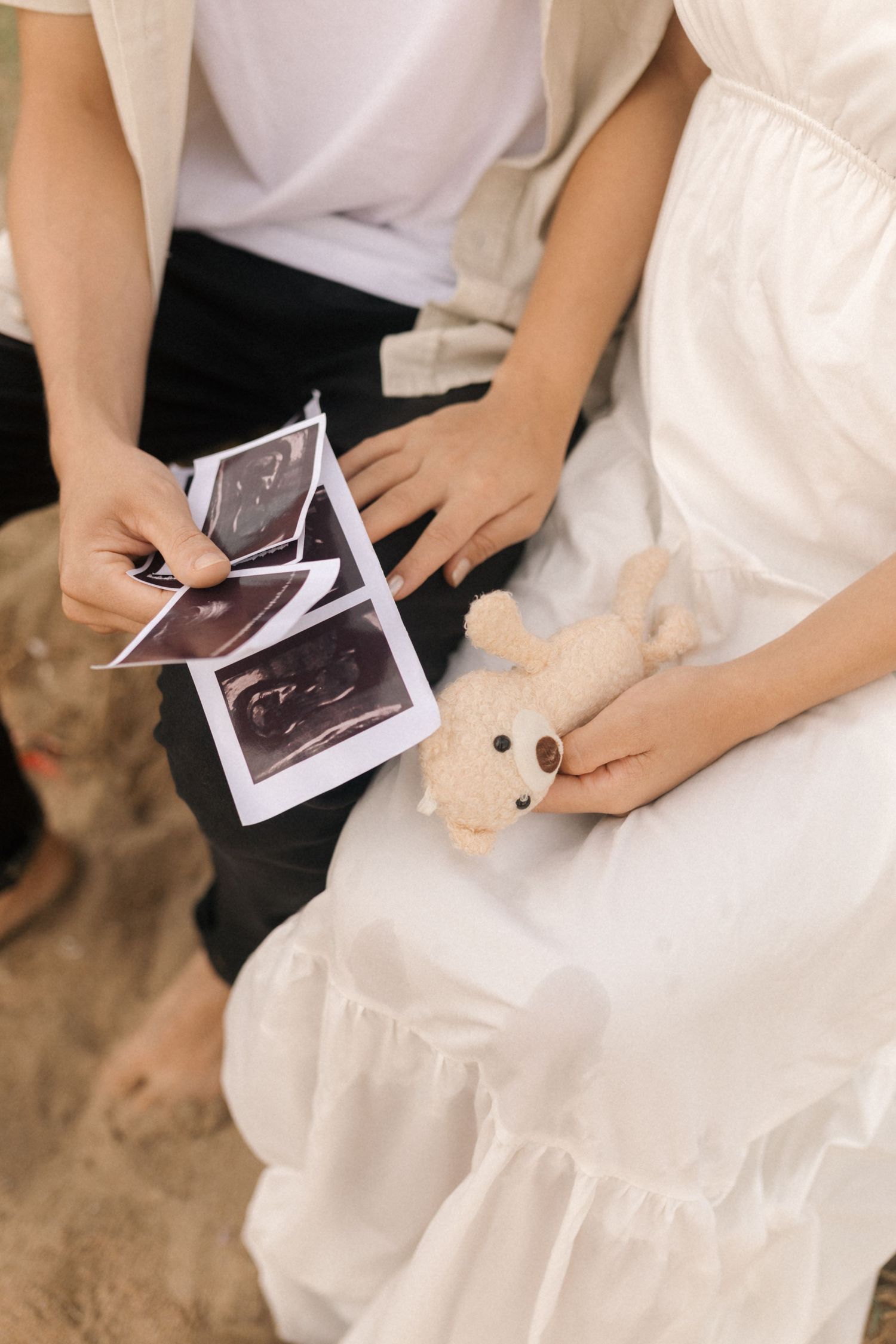 Close-up shots of hands holding ultrasound photos while sitting on a sandy surface.