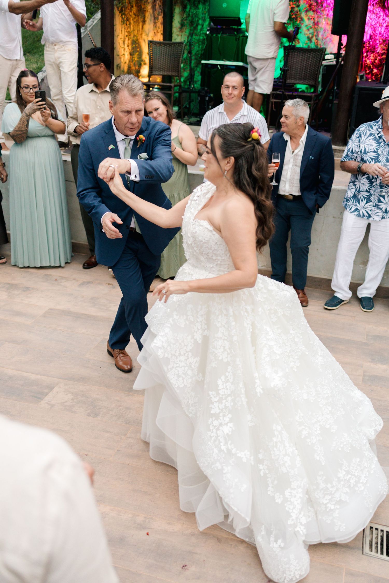 Couple dancing on stone patio during wedding reception with guests watching.