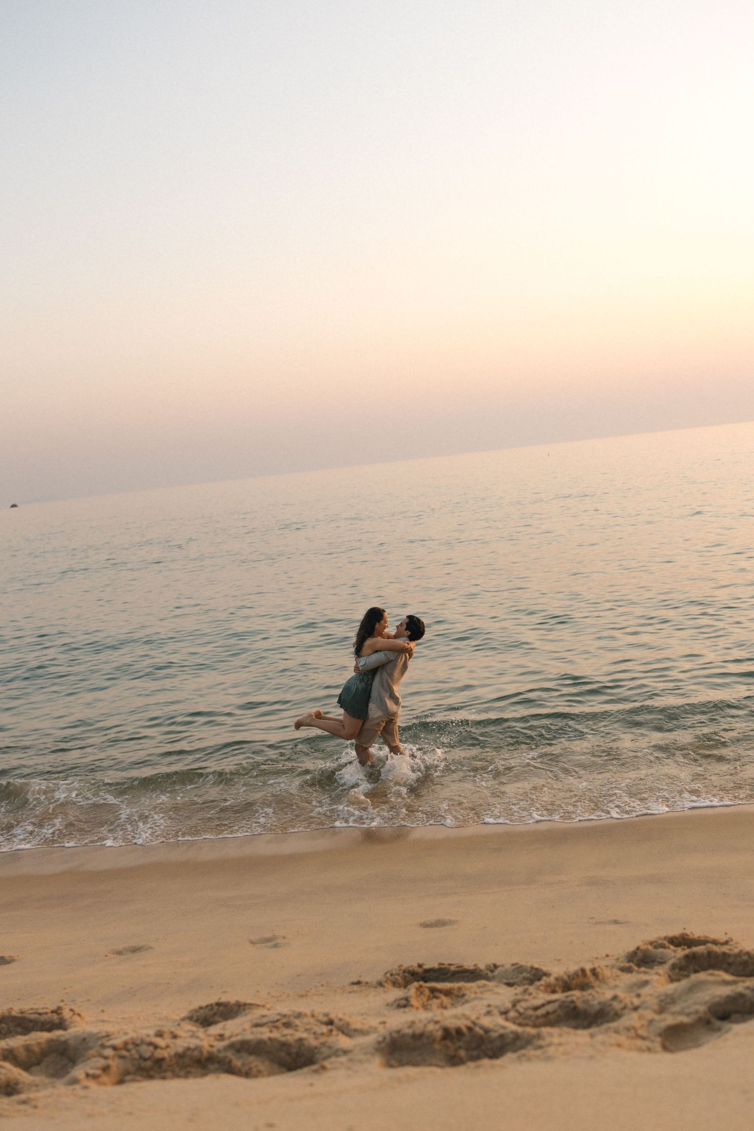 People running and splashing through shallow beach waves during a serene sunset.
