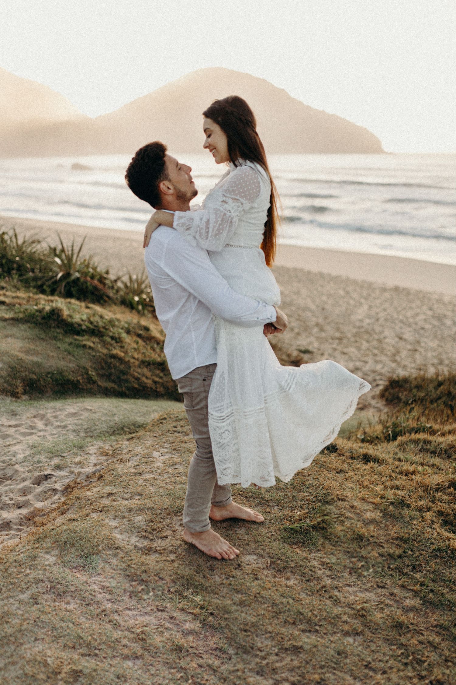 Romantic seaside photoshoot of couple dancing on grassy slope.