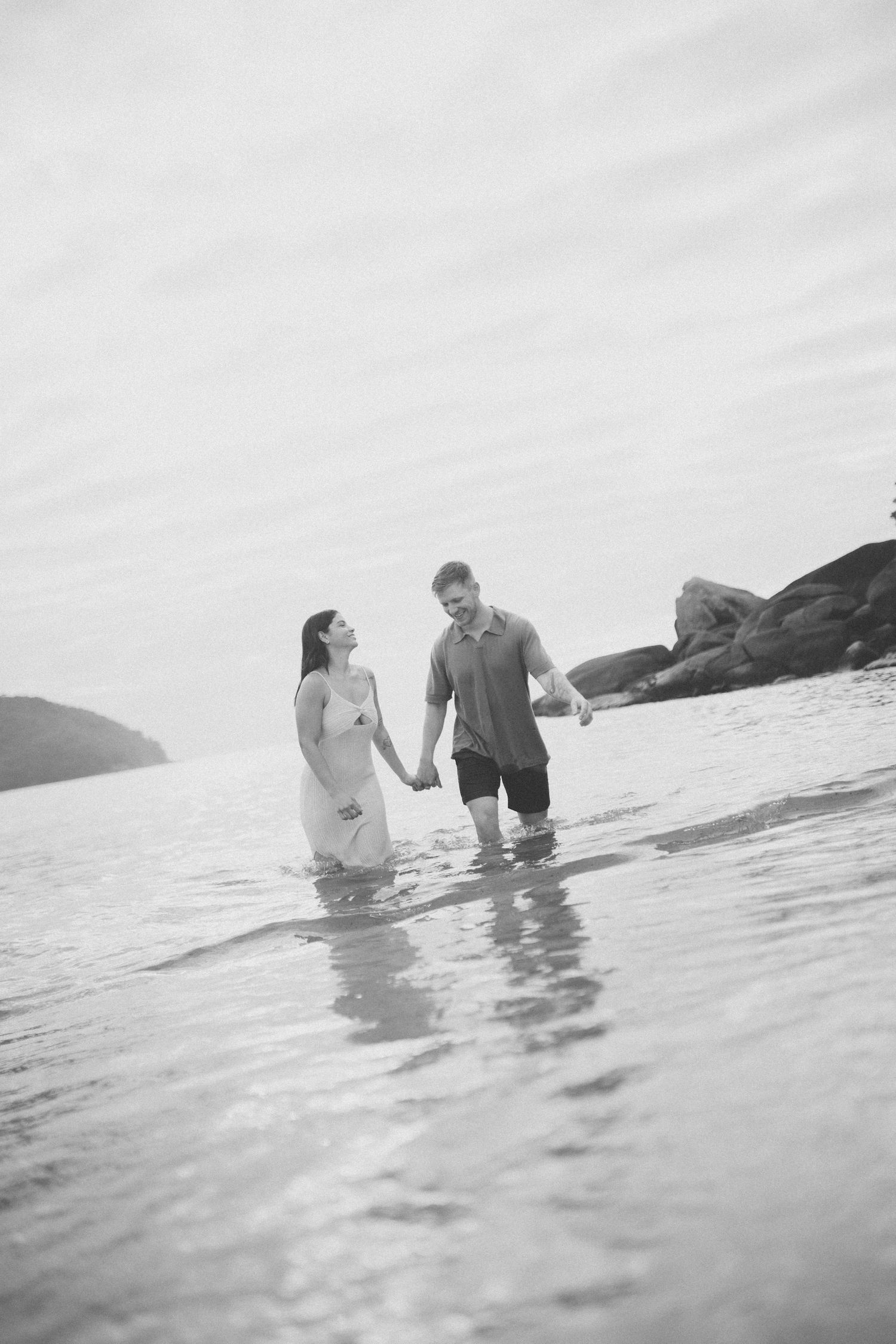 A couple shares an intimate moment while standing in the ocean waters near a rocky shore.