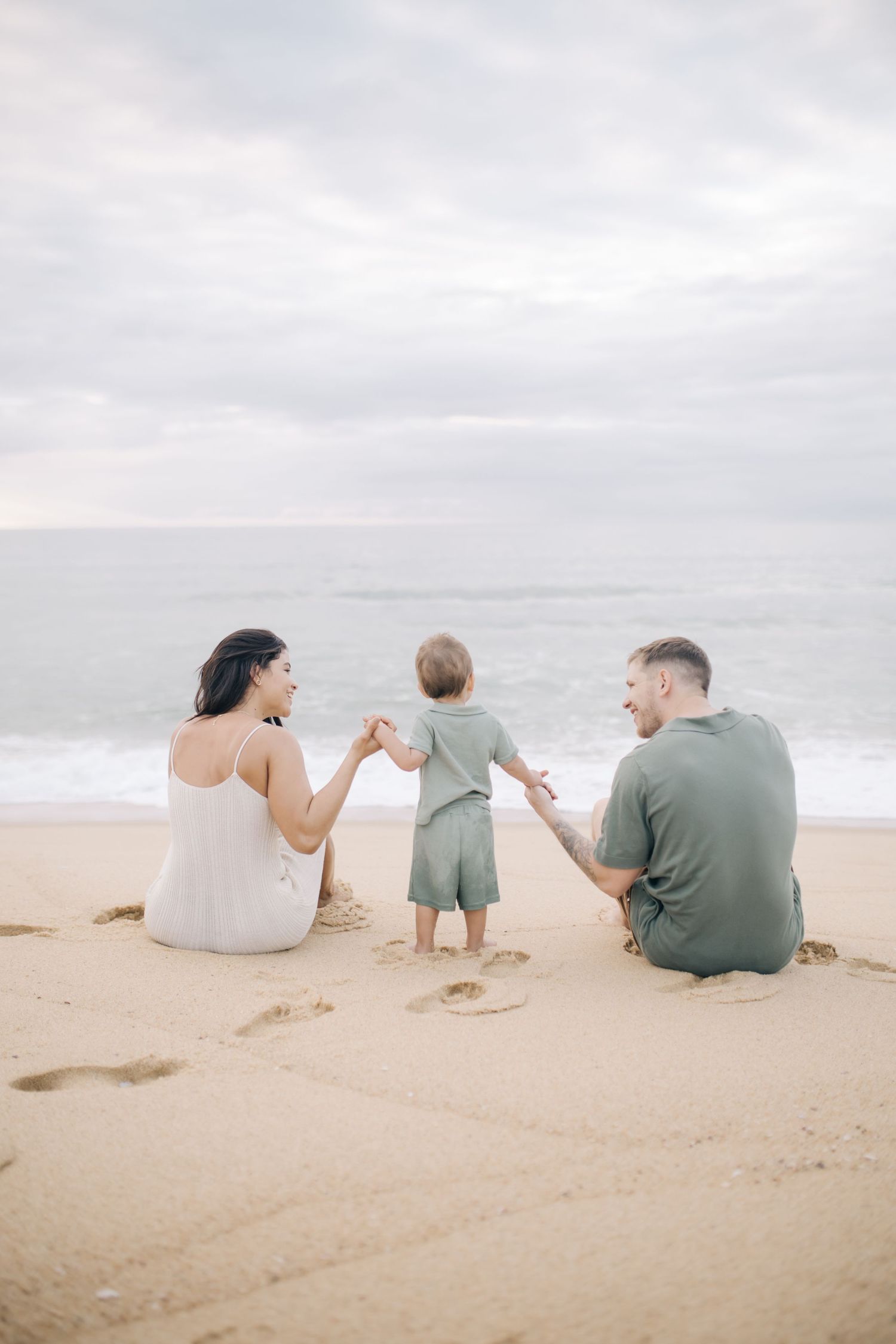 Family sitting together on sandy beach watching the ocean waves roll in.