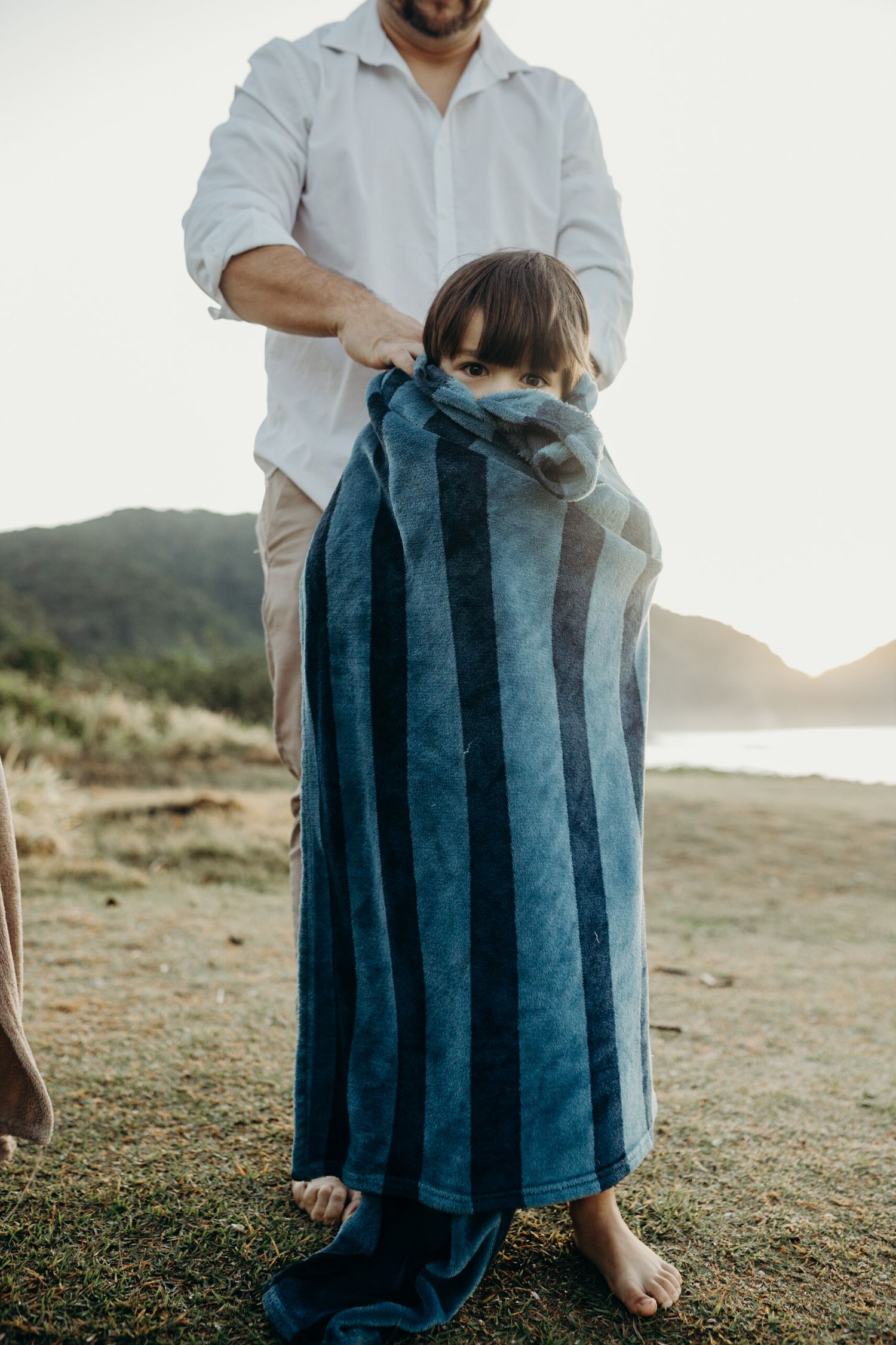 Blue striped beach towel being held up against coastal landscape at sunset.