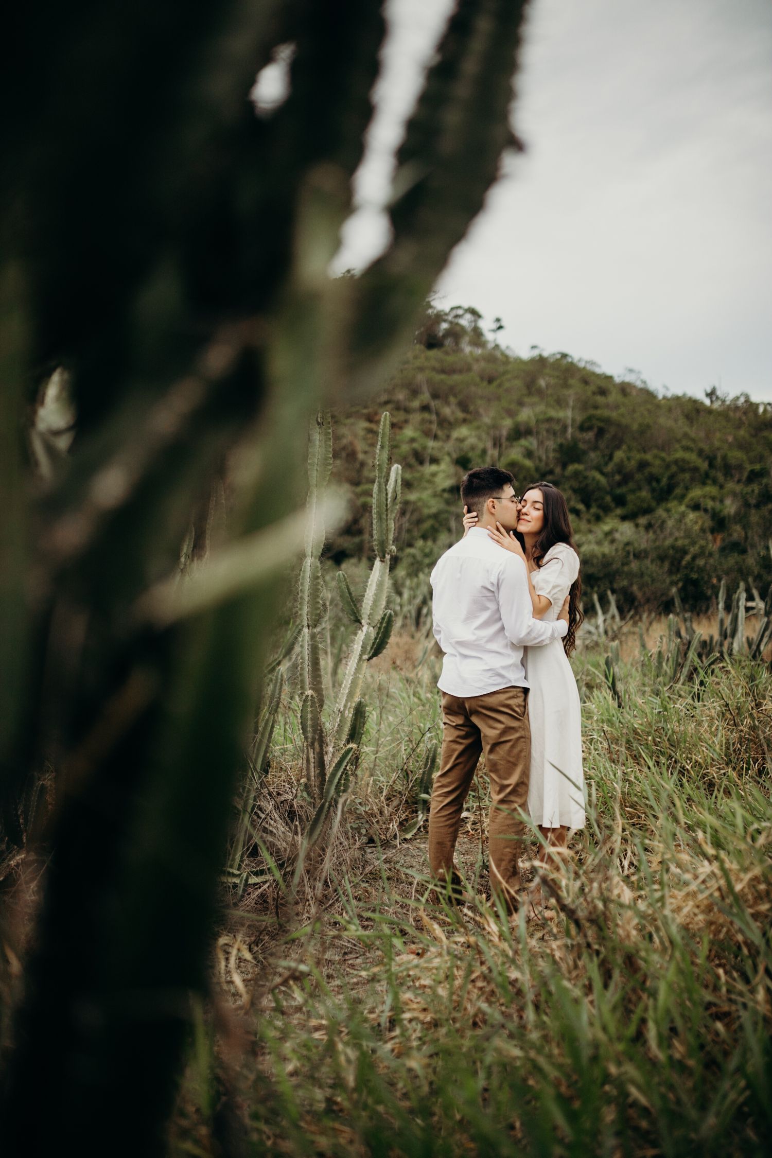 Intimate portrait of couple among tall grass with mountain backdrop.