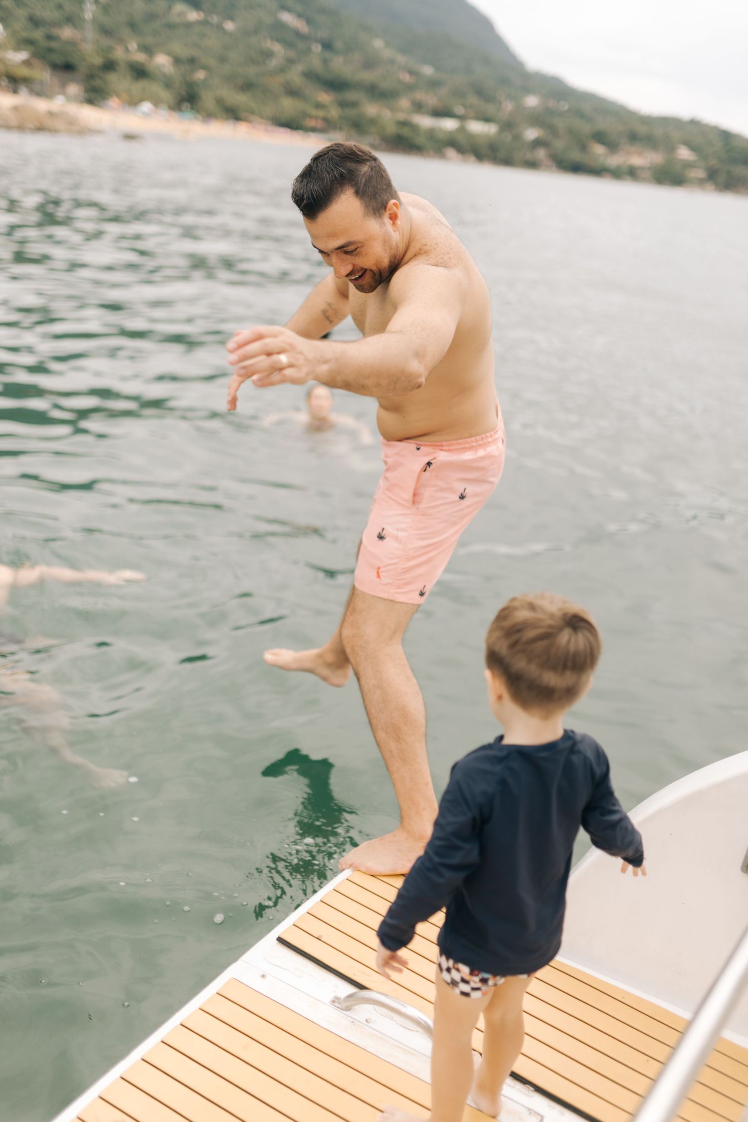 Parent and child preparing to jump together from wooden boat deck into water.