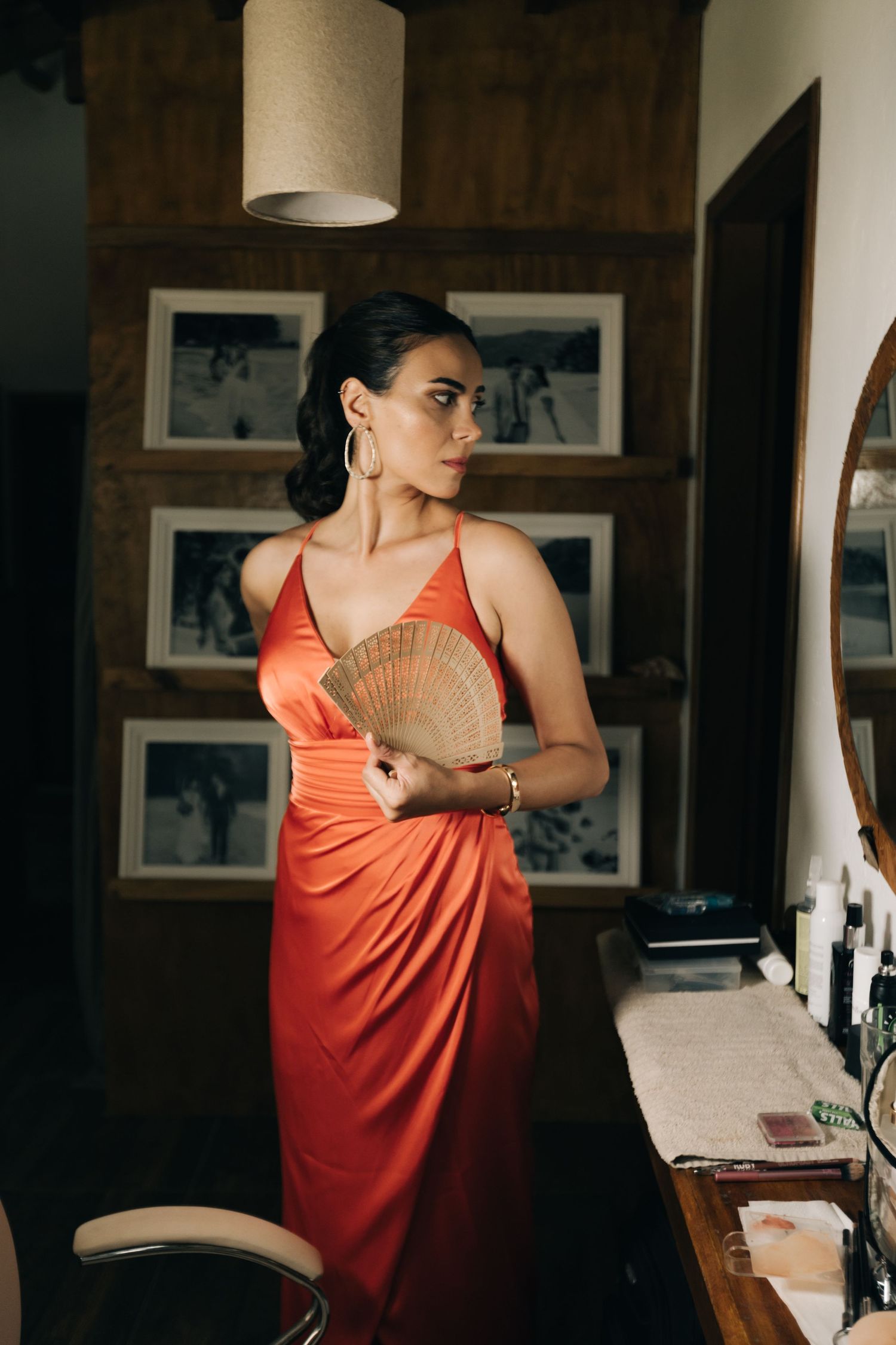 Woman in coral evening dress holding decorative fan in dimly lit room.