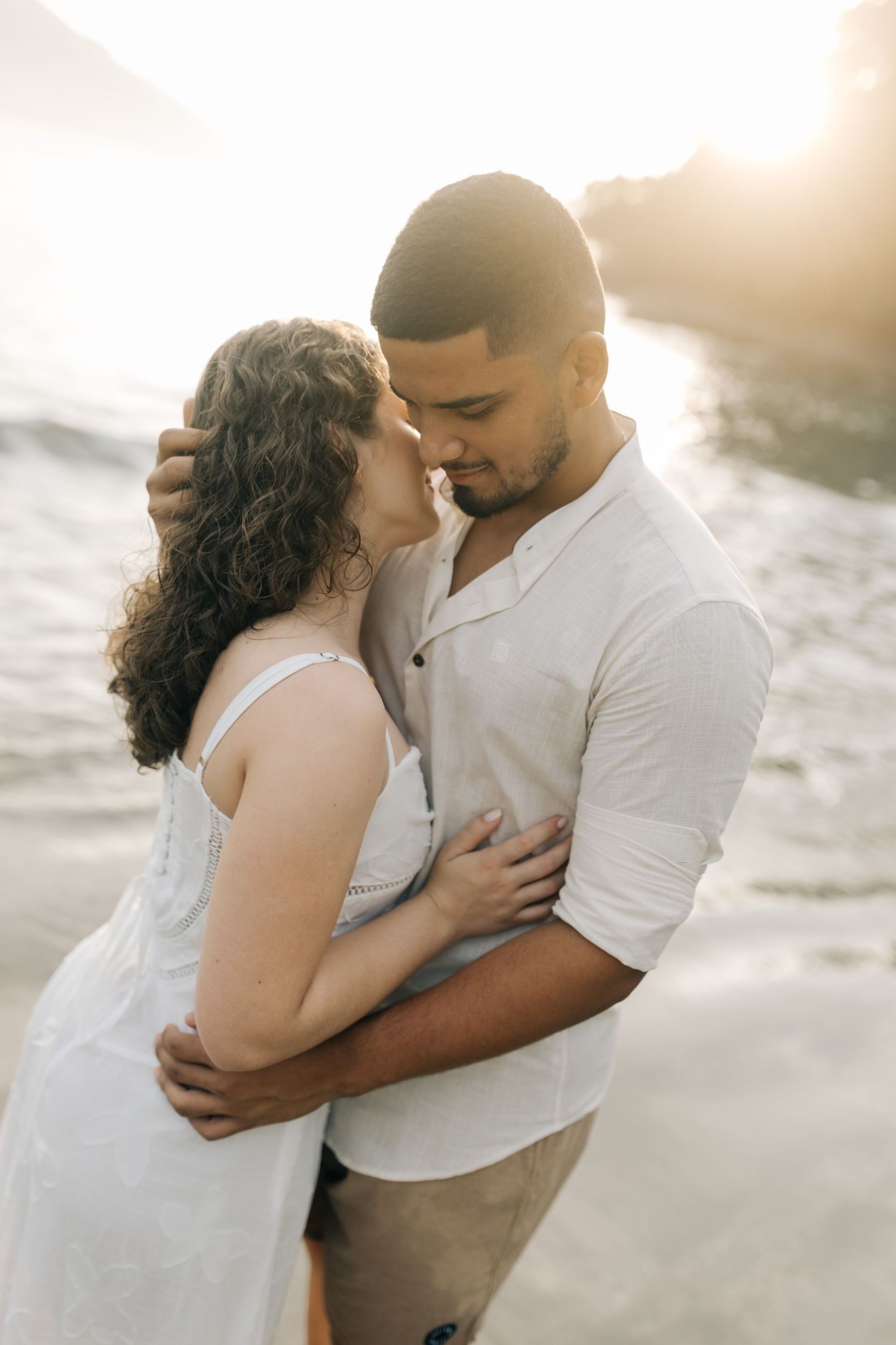 Intimate beach portraits of a couple in white outfits during golden hour.