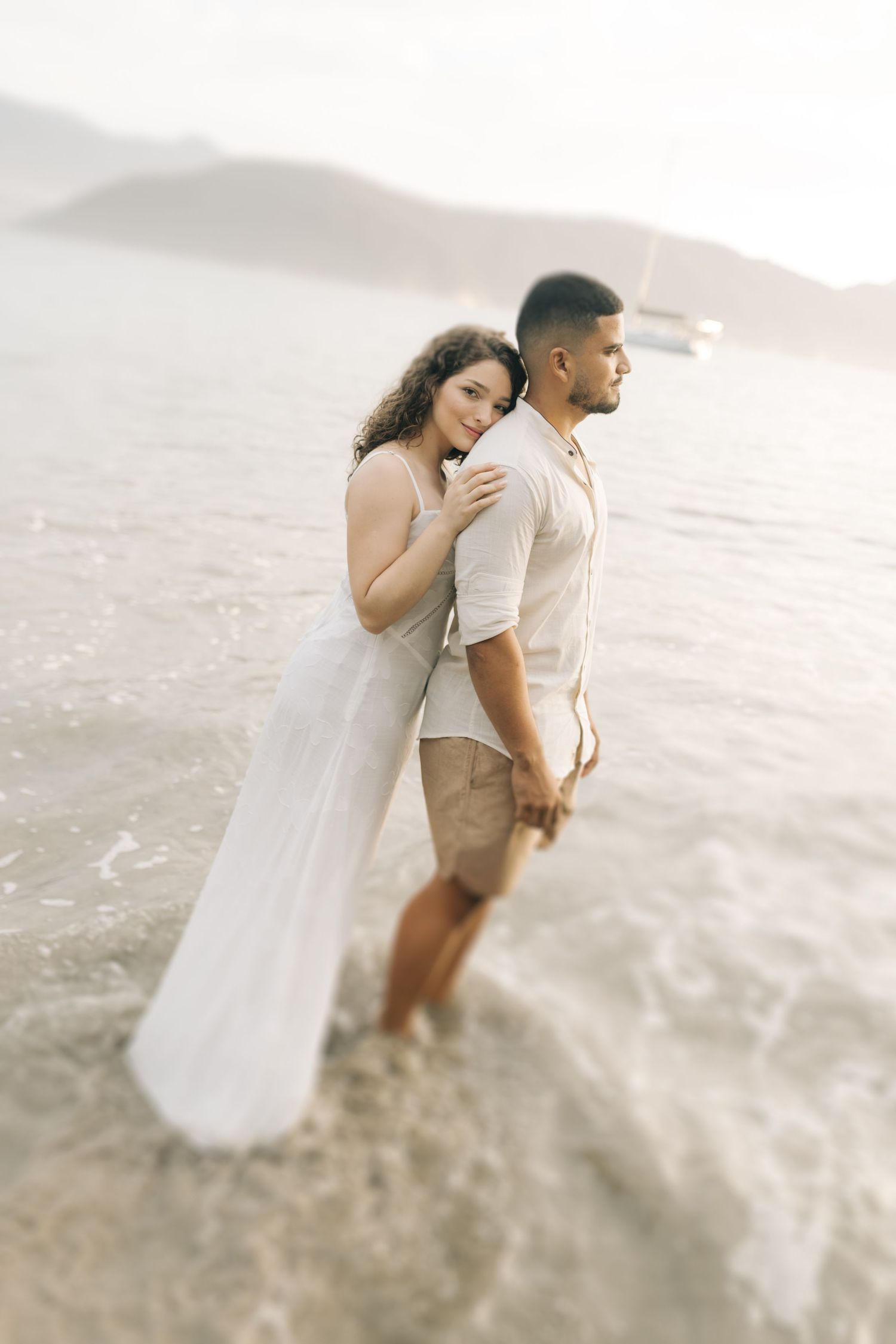 A couple stands in shallow ocean water during a romantic beach photo session.