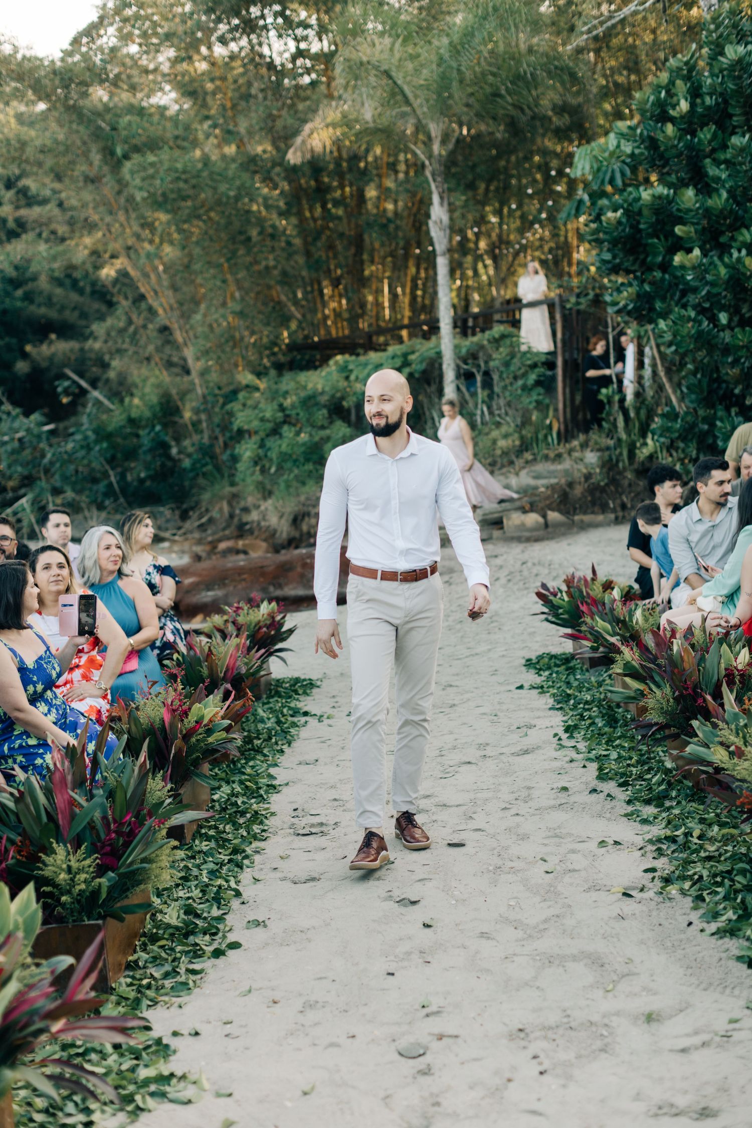 Wedding guests watching as attendants walk down a sandy outdoor aisle.