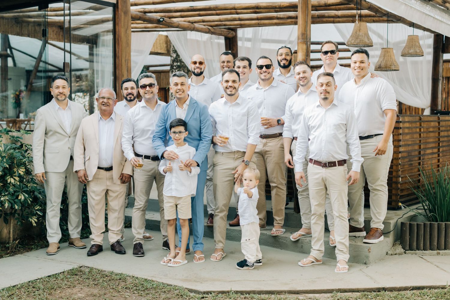 Wedding party group photo with men wearing light colored suits outdoors.