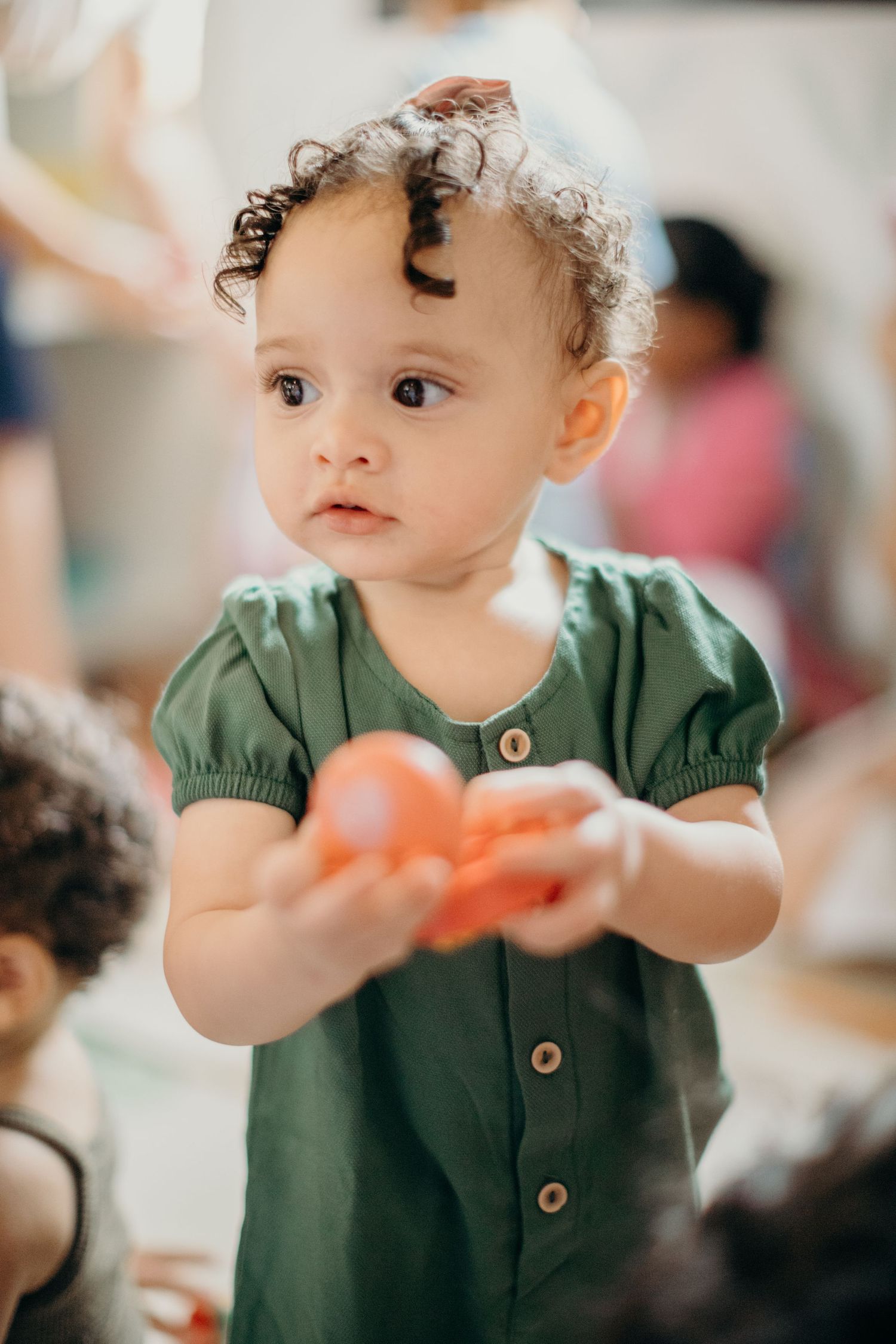 Small child in green dress playing with toys during indoor activity.