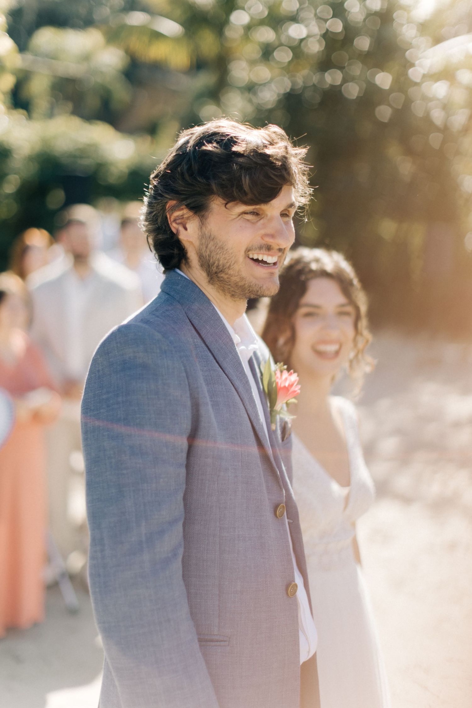 A sunny beach wedding ceremony with guests watching in the background.