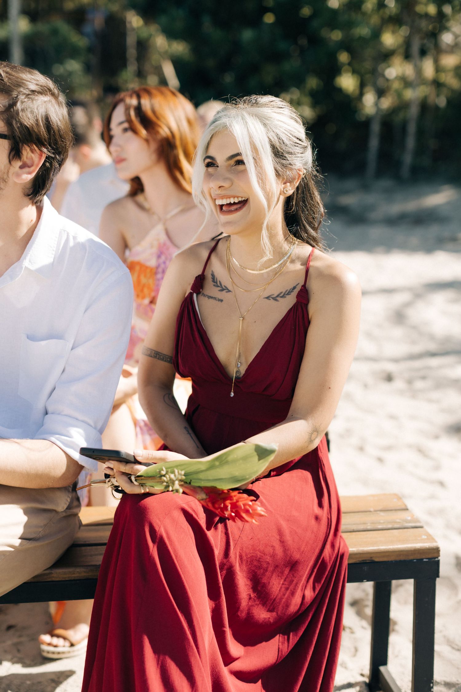 Guests in red dresses smile during an outdoor wedding celebration.