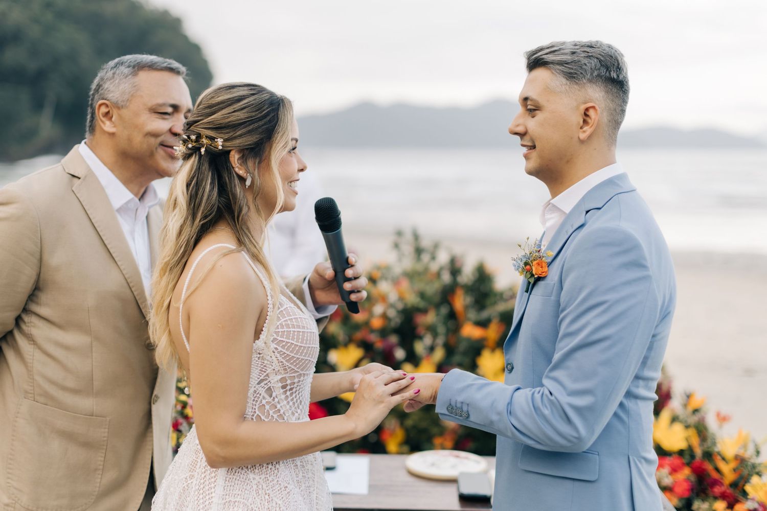 Candid moment during beach wedding ceremony with light blue and tan suited officiants.