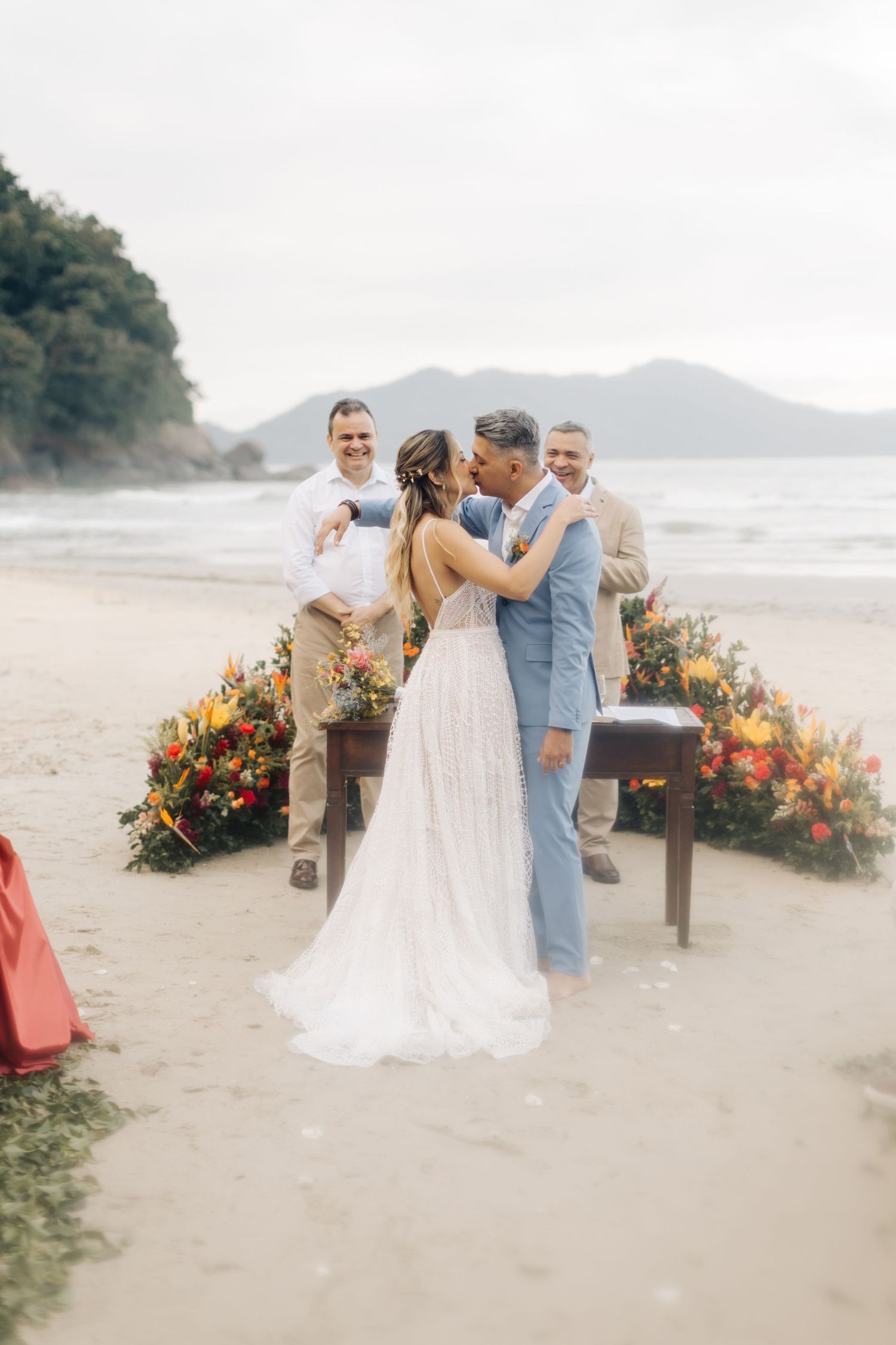 Beach wedding ceremony setup with vibrant orange and yellow floral arrangements on wooden stands.