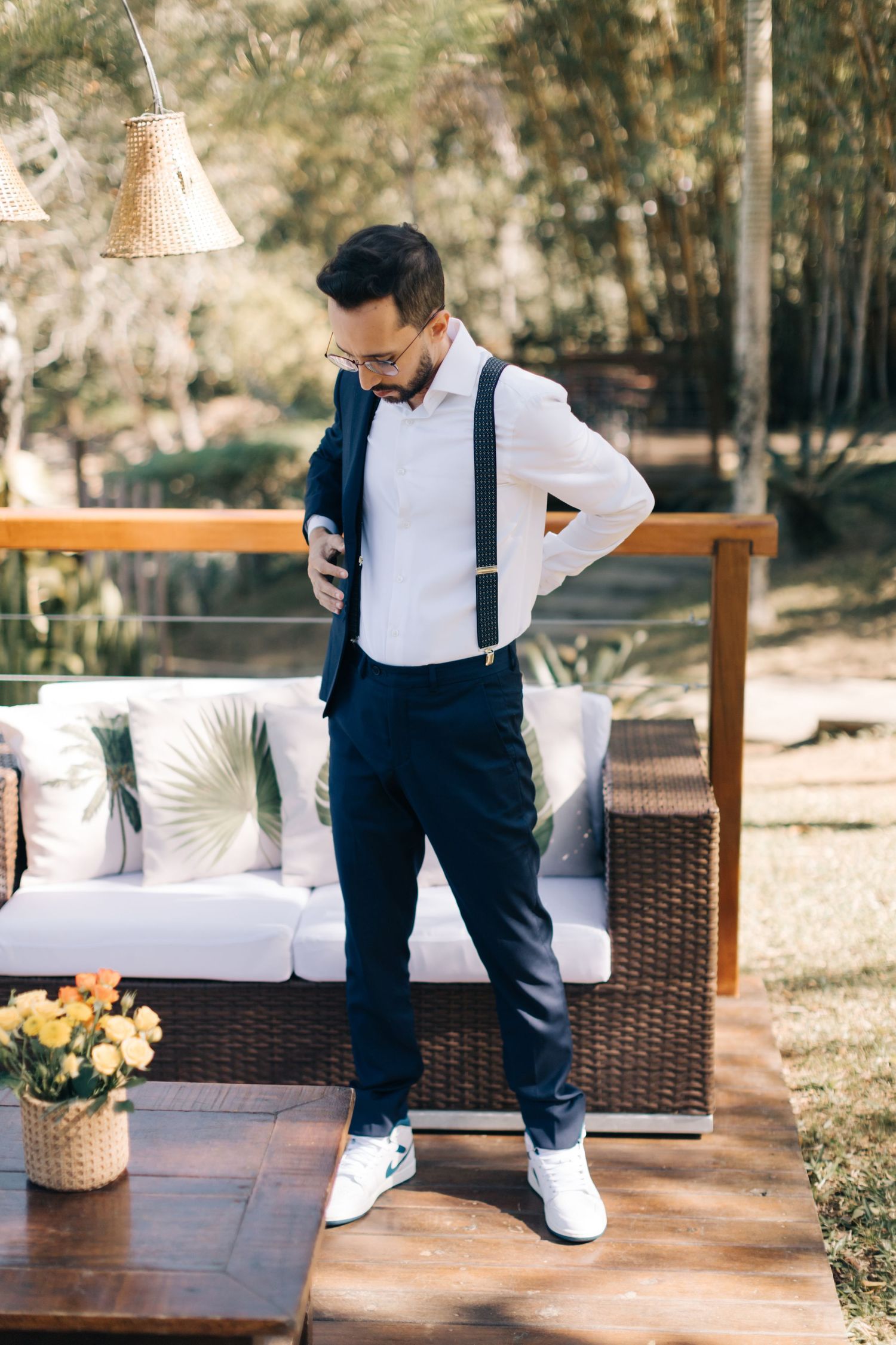 Stylish groom in navy suspenders and white shirt on outdoor patio.