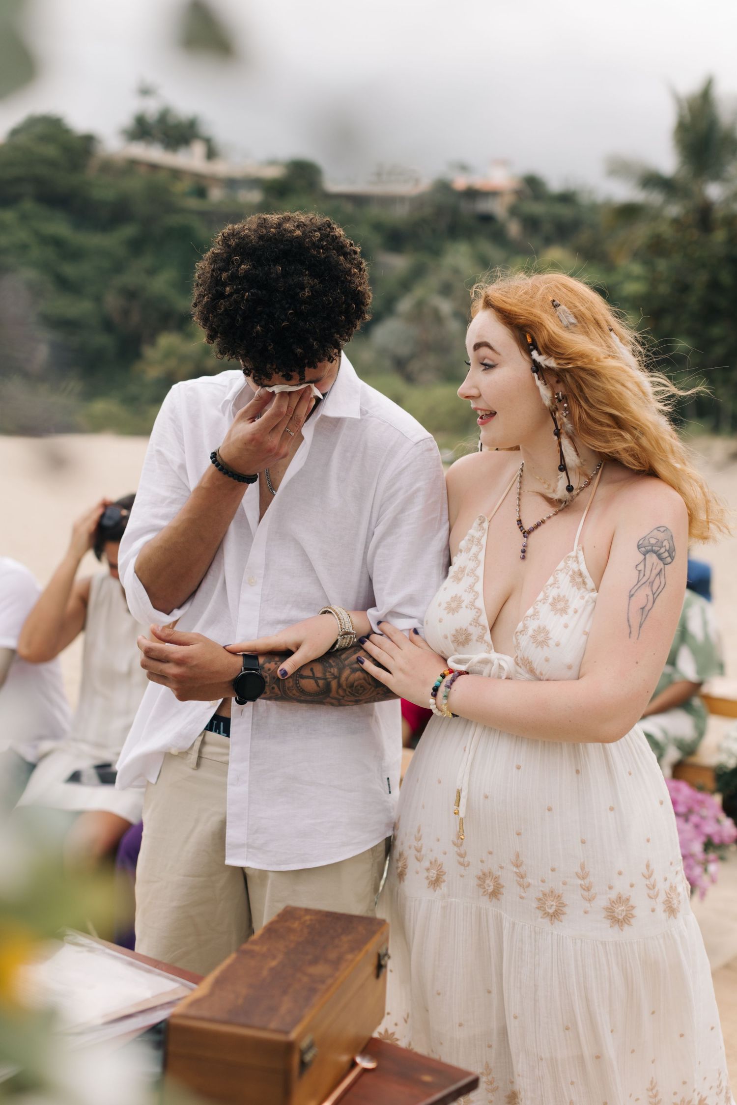A candid emotional moment during a beach wedding ceremony with floral decorations.
