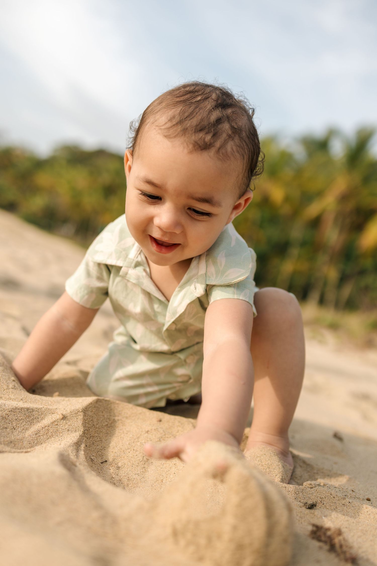 Small child playing and crawling in soft beach sand on a sunny day.
