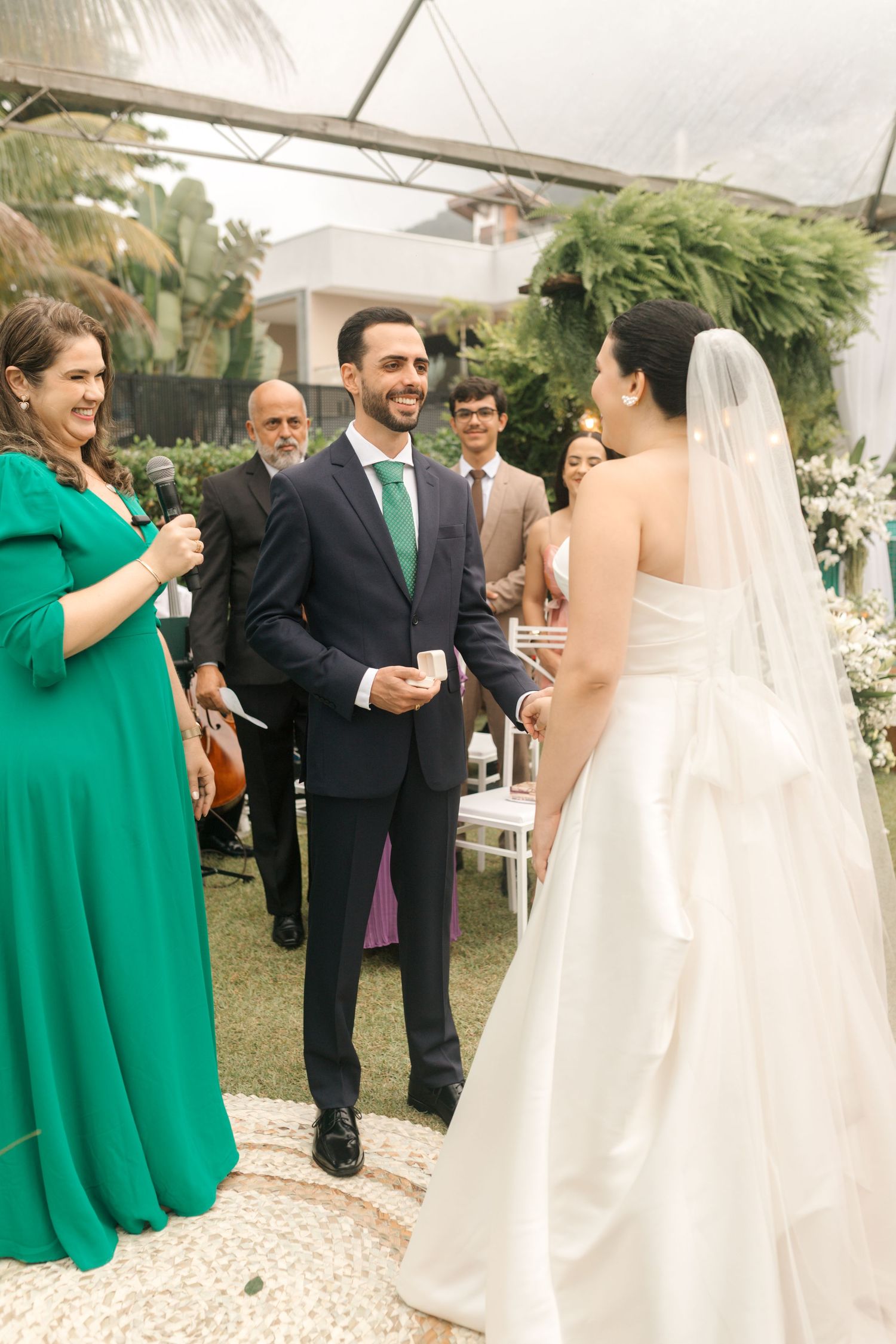 Wedding party mingling during outdoor reception with white tent and greenery.