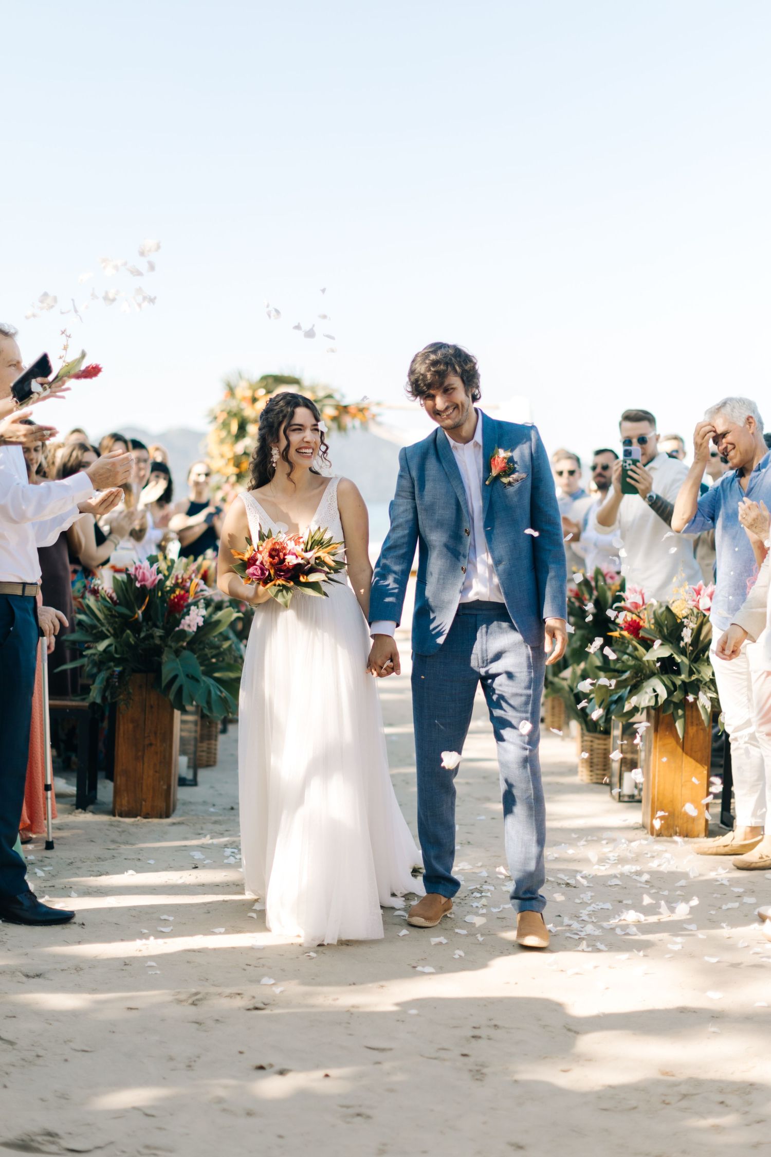 A romantic beach wedding ceremony with newlyweds walking down the aisle while guests throw flower petals.
