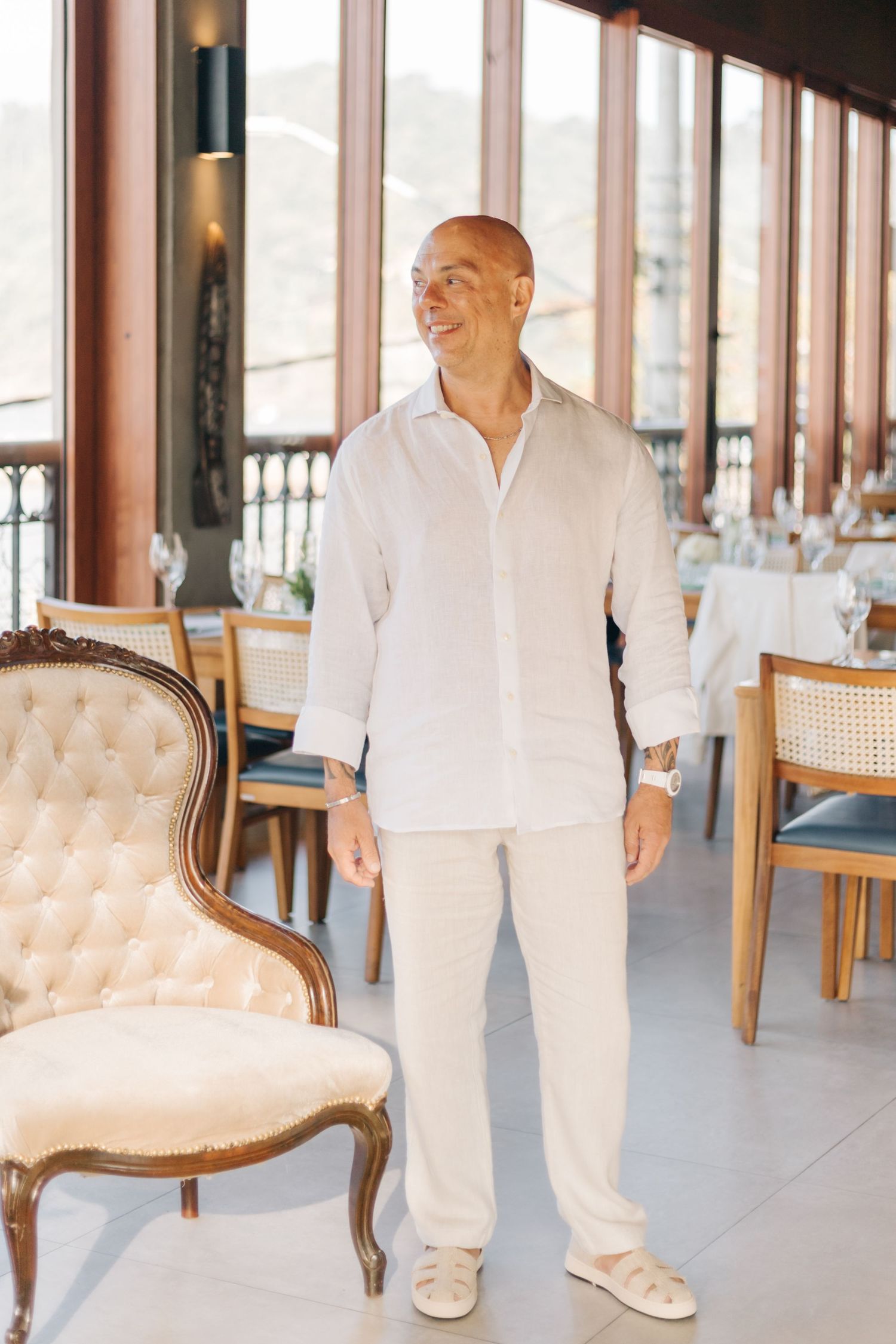 Person in all white clothing walking through an elegant room with vintage tufted chairs.