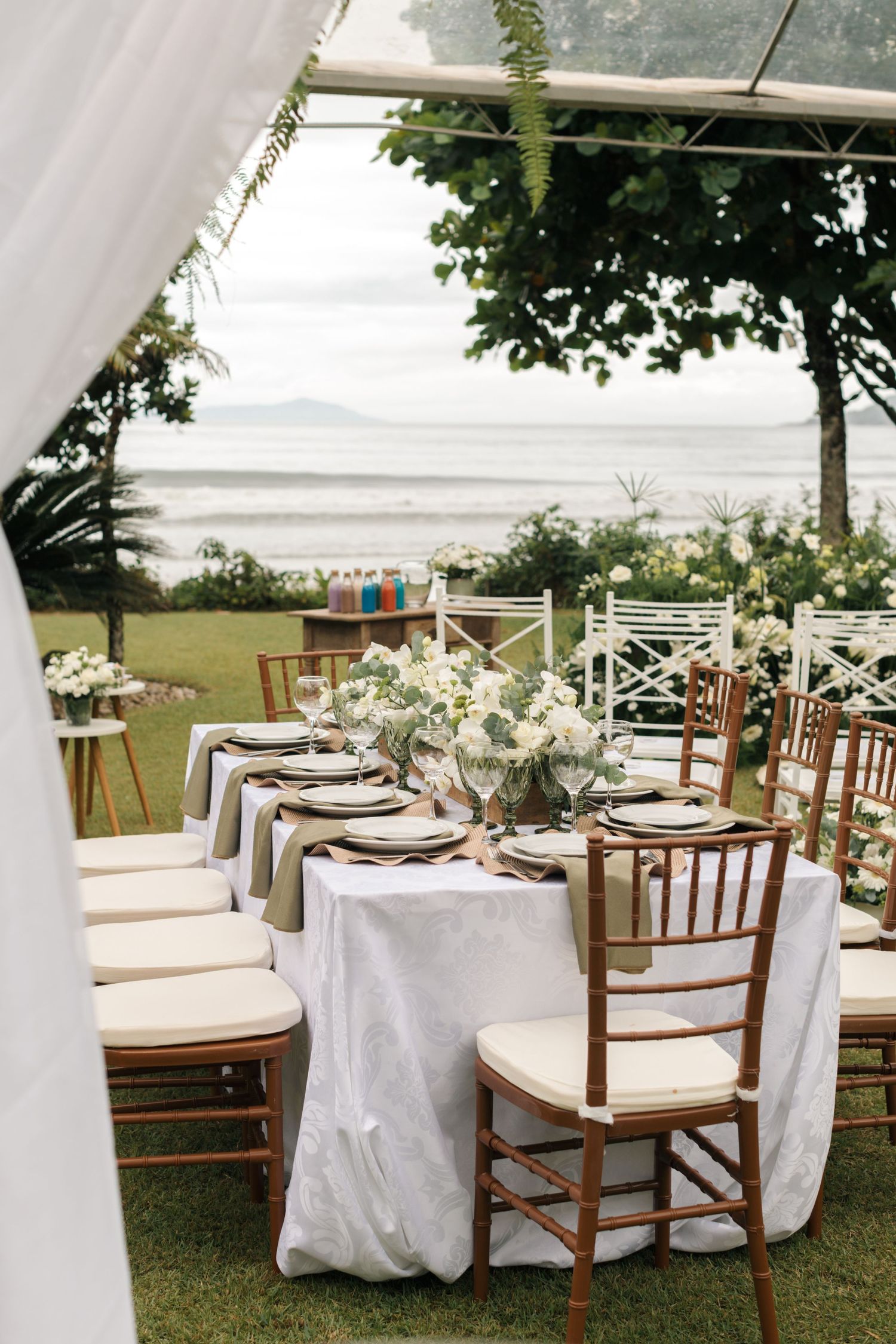 Elegant outdoor wedding table setting with white linens and wooden chairs overlooking ocean view.