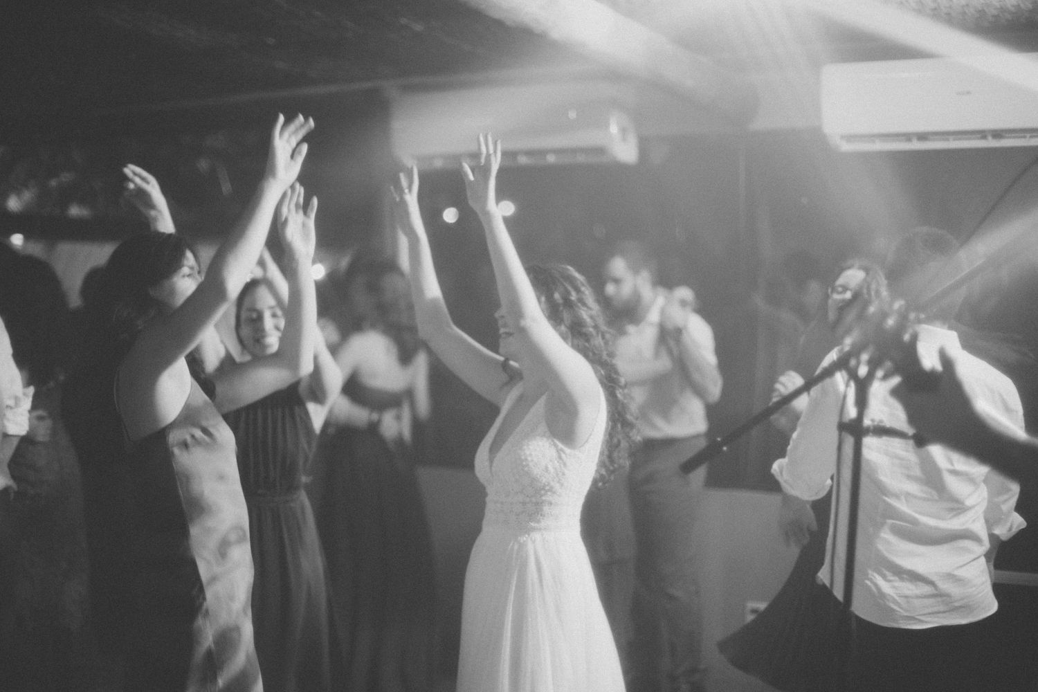 Guests with raised arms dancing under atmospheric lighting at a wedding celebration.