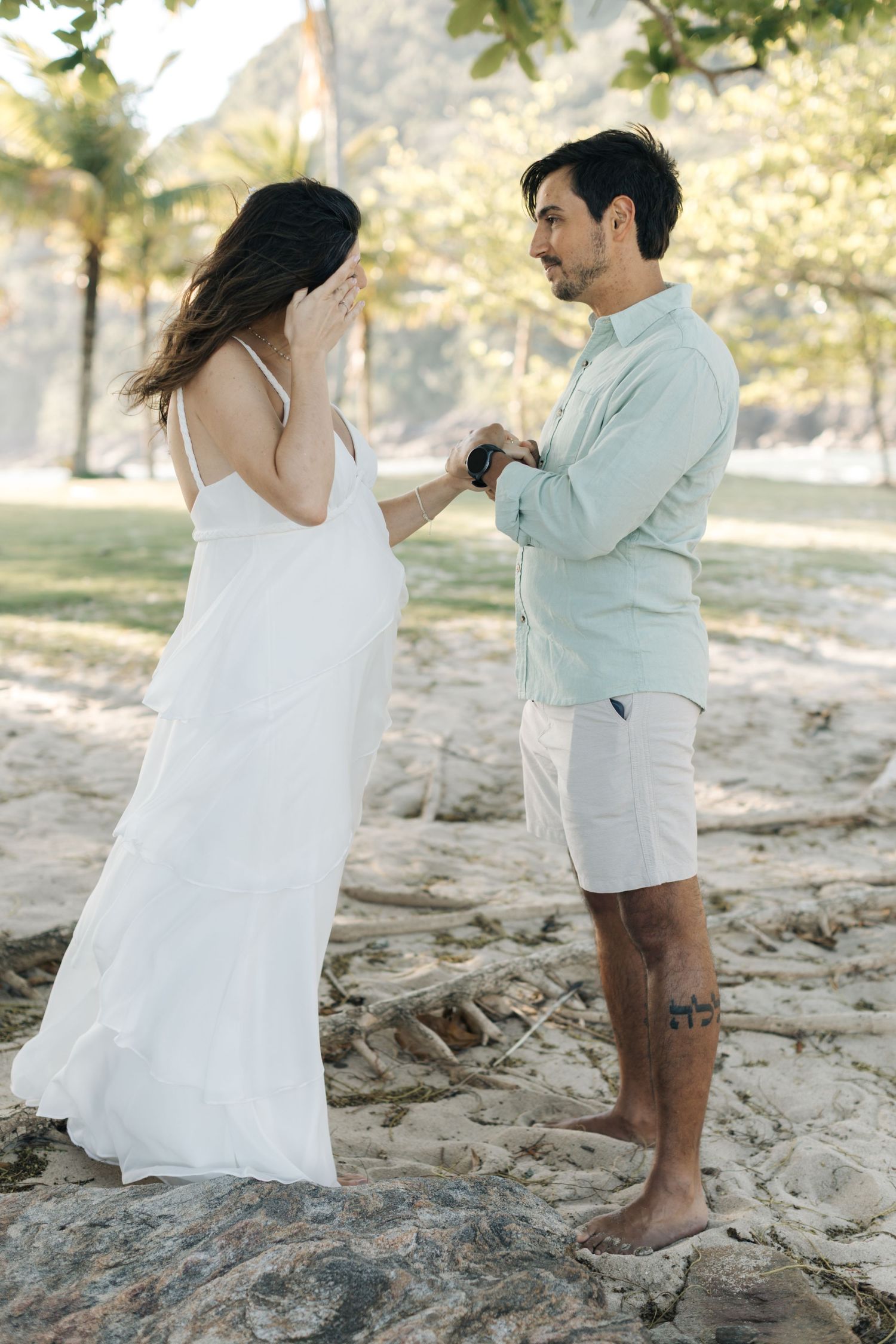A couple in white and mint clothing dances together on a rocky beach landscape.