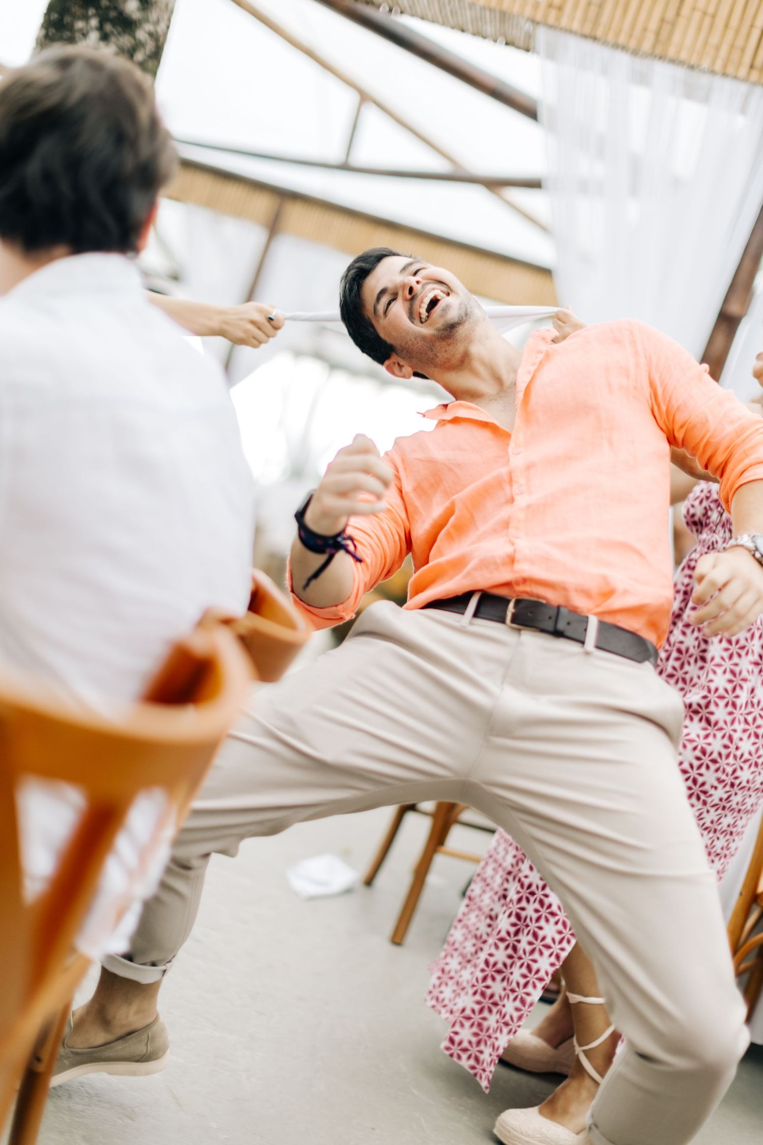 Wedding guest in orange shirt laughs joyfully while dancing at reception celebration.