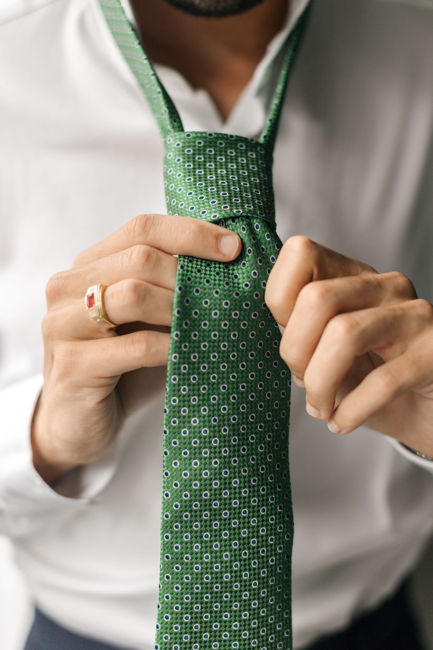 Close-up of hands adjusting an emerald green patterned tie with a wedding ring visible.