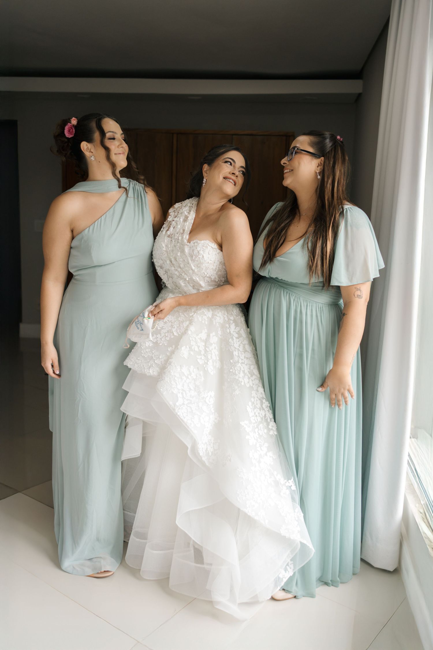 Bridesmaids in mint green dresses gather around a bride in a white lace gown during wedding preparations.