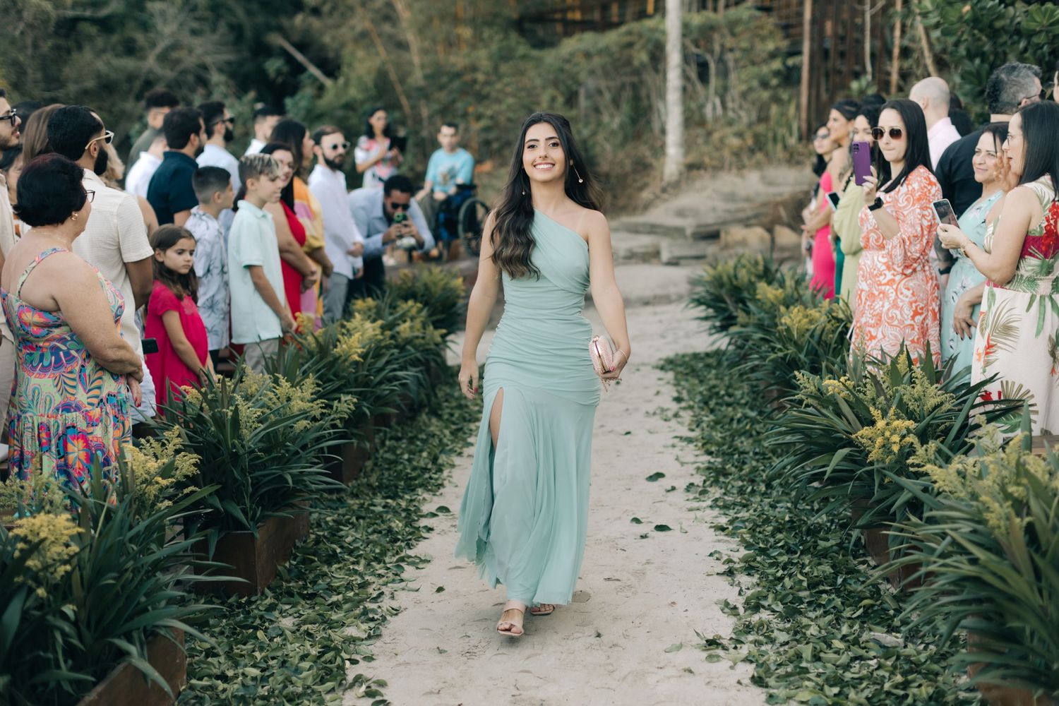Wedding guests mingle on a garden path surrounded by lush greenery.