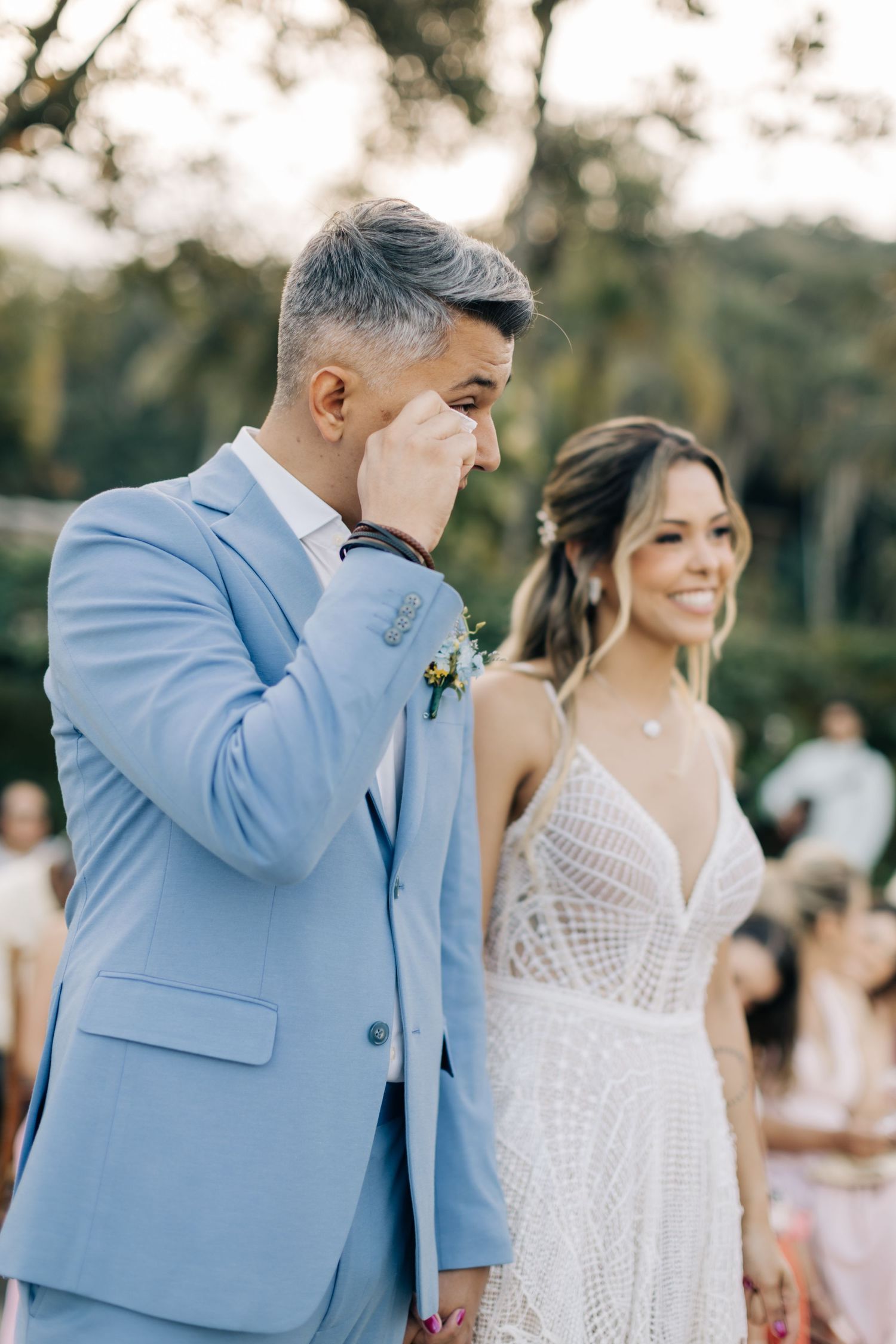 Emotional moment in light blue suit and white lace dress at beach wedding ceremony.