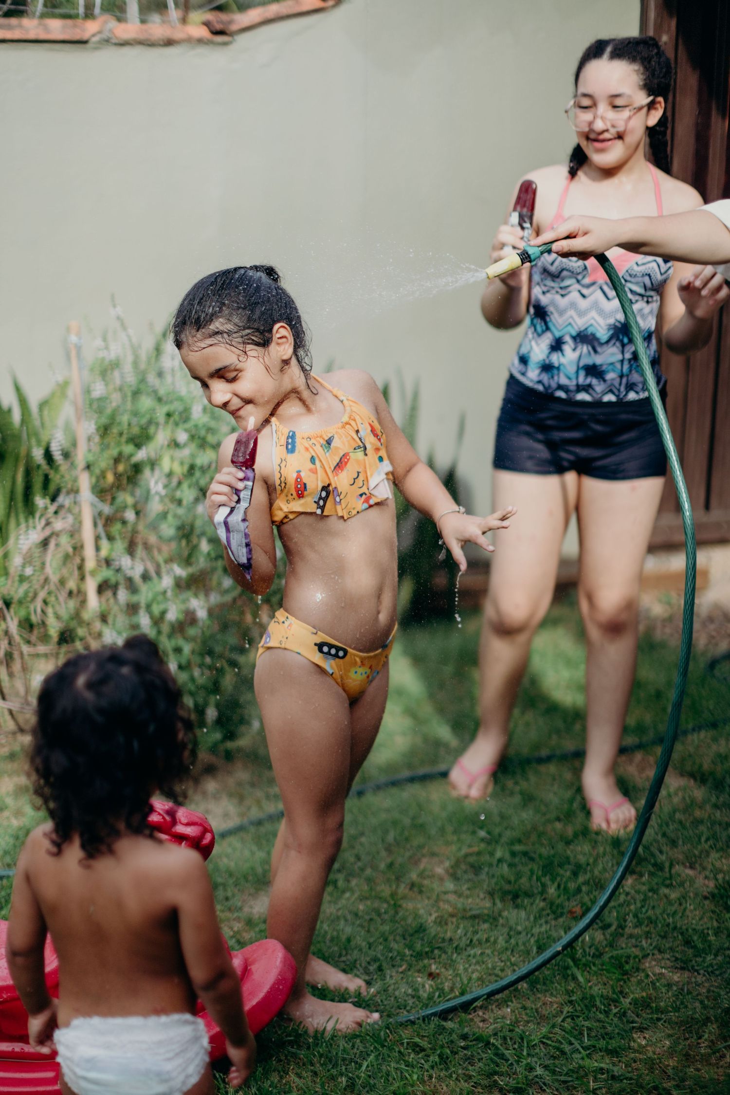 Children playing with a water hose in the garden wearing colorful swimsuits.