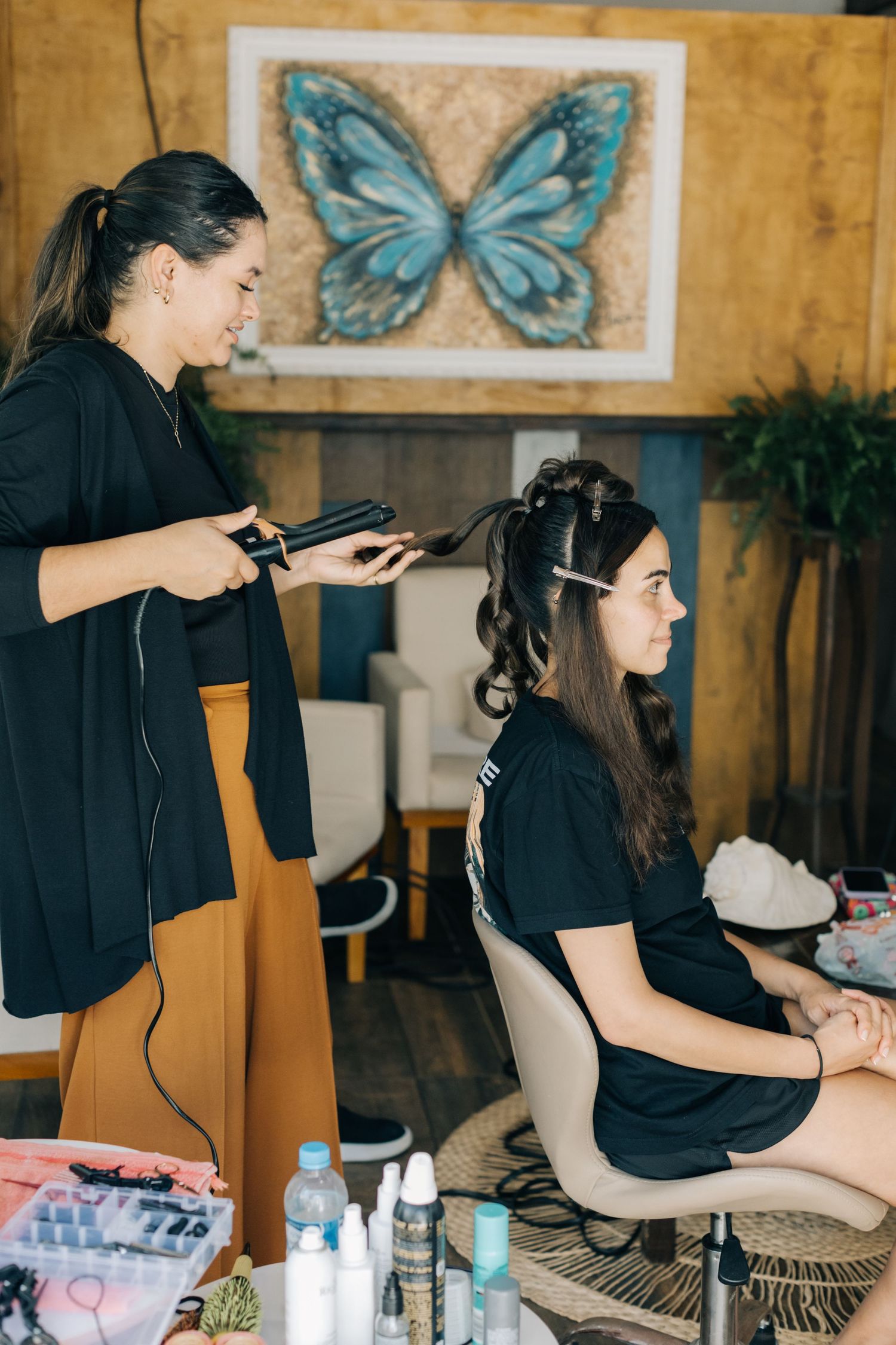 Hair styling session in progress with butterfly artwork visible on wooden walls.