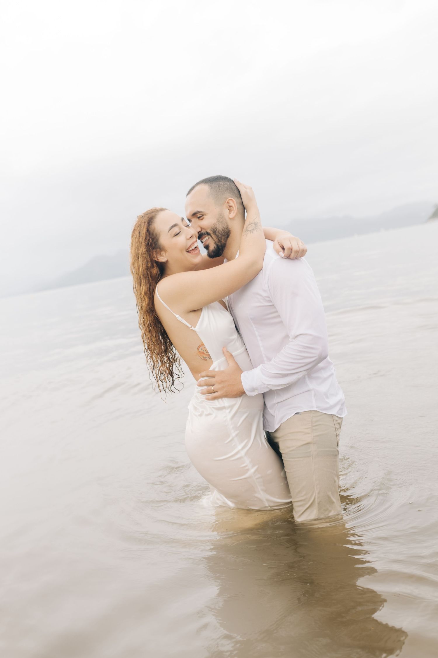 A joyful couple laughs while embracing in knee-deep ocean water.